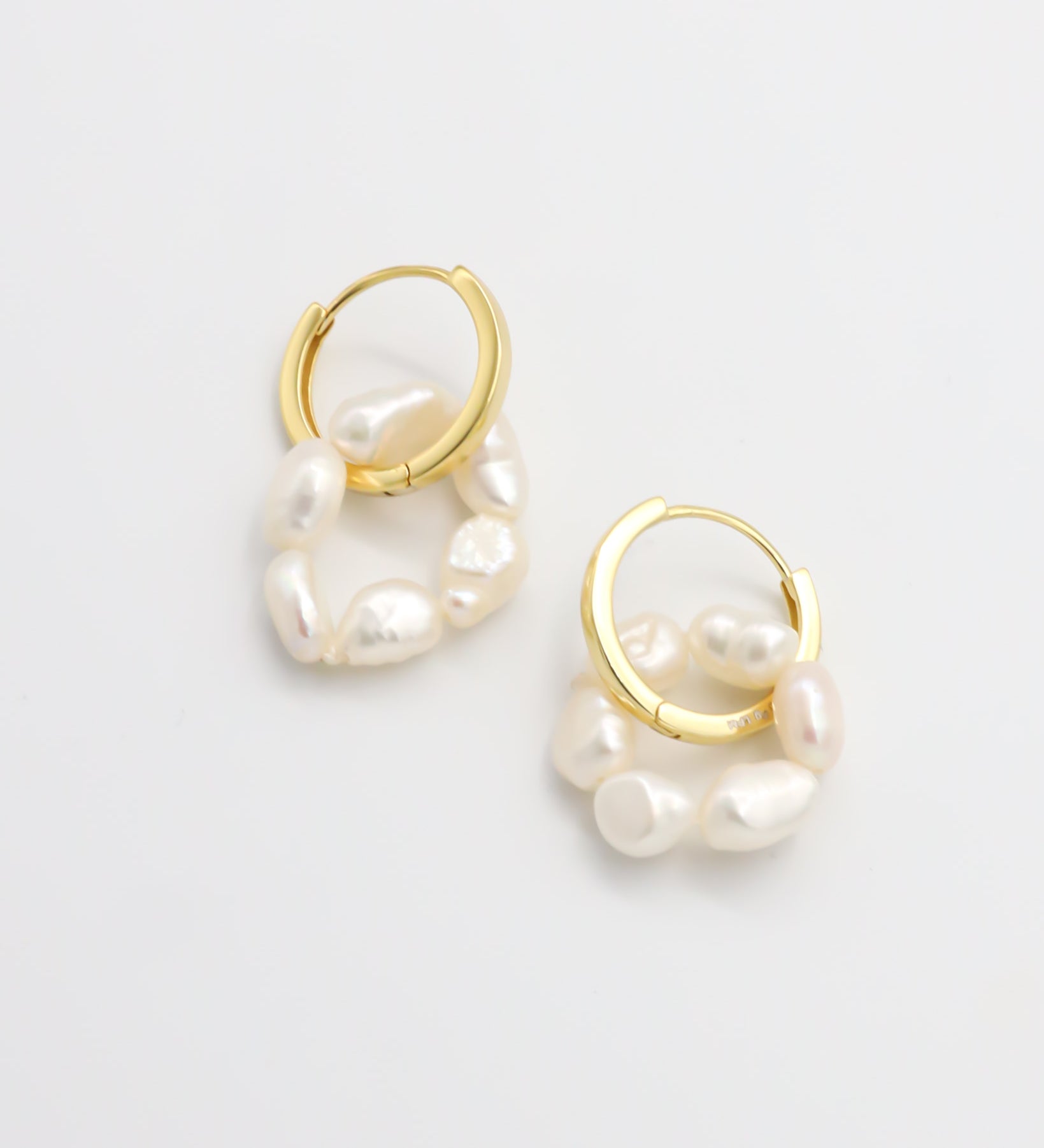 A pair of gold hoop earrings with white pearls attached to them, displayed on a white background.