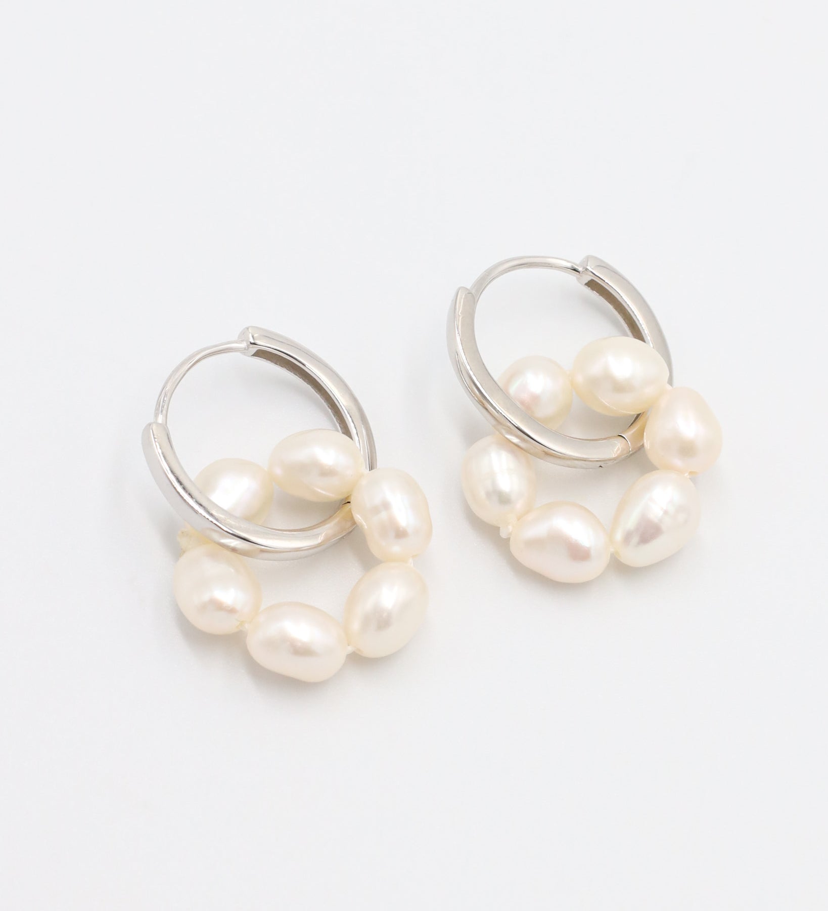 A pair of silver hoop earrings with white pearls attached to them, displayed on a white background.