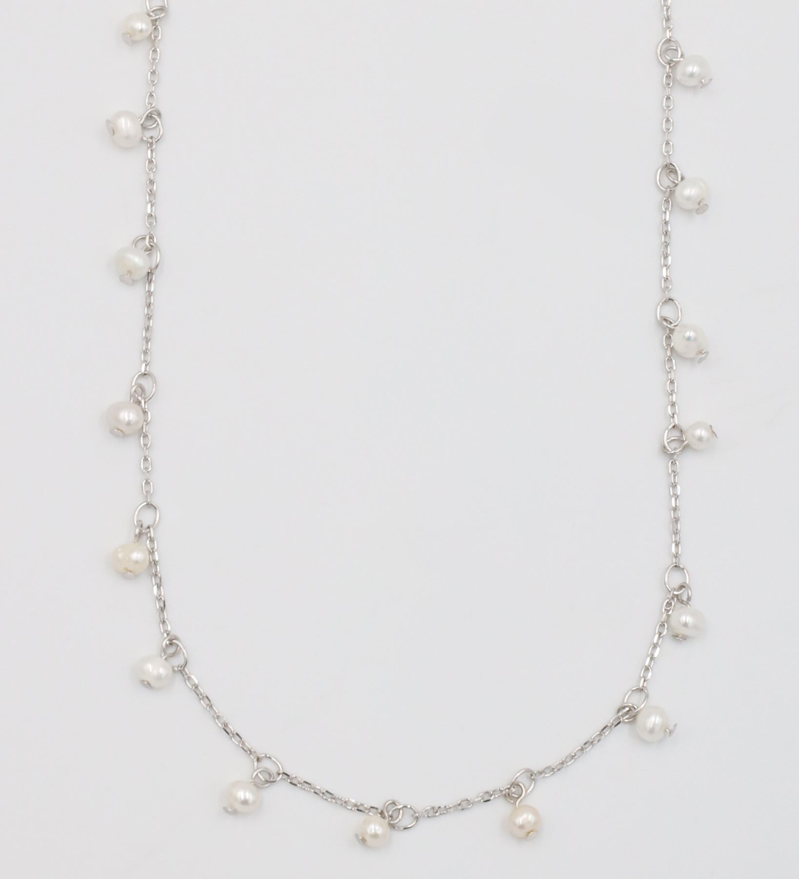 A silver necklace with a series of small pearls scattered along a chain, displayed against a white background.