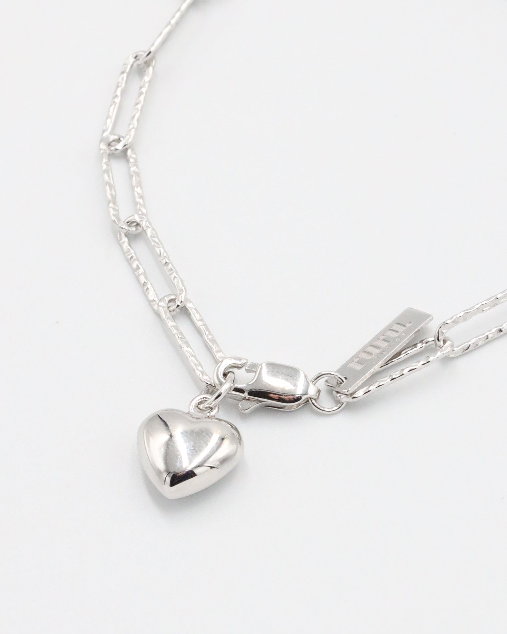 A silver bracelet with a heart-shaped charm on a white background - Close Up.