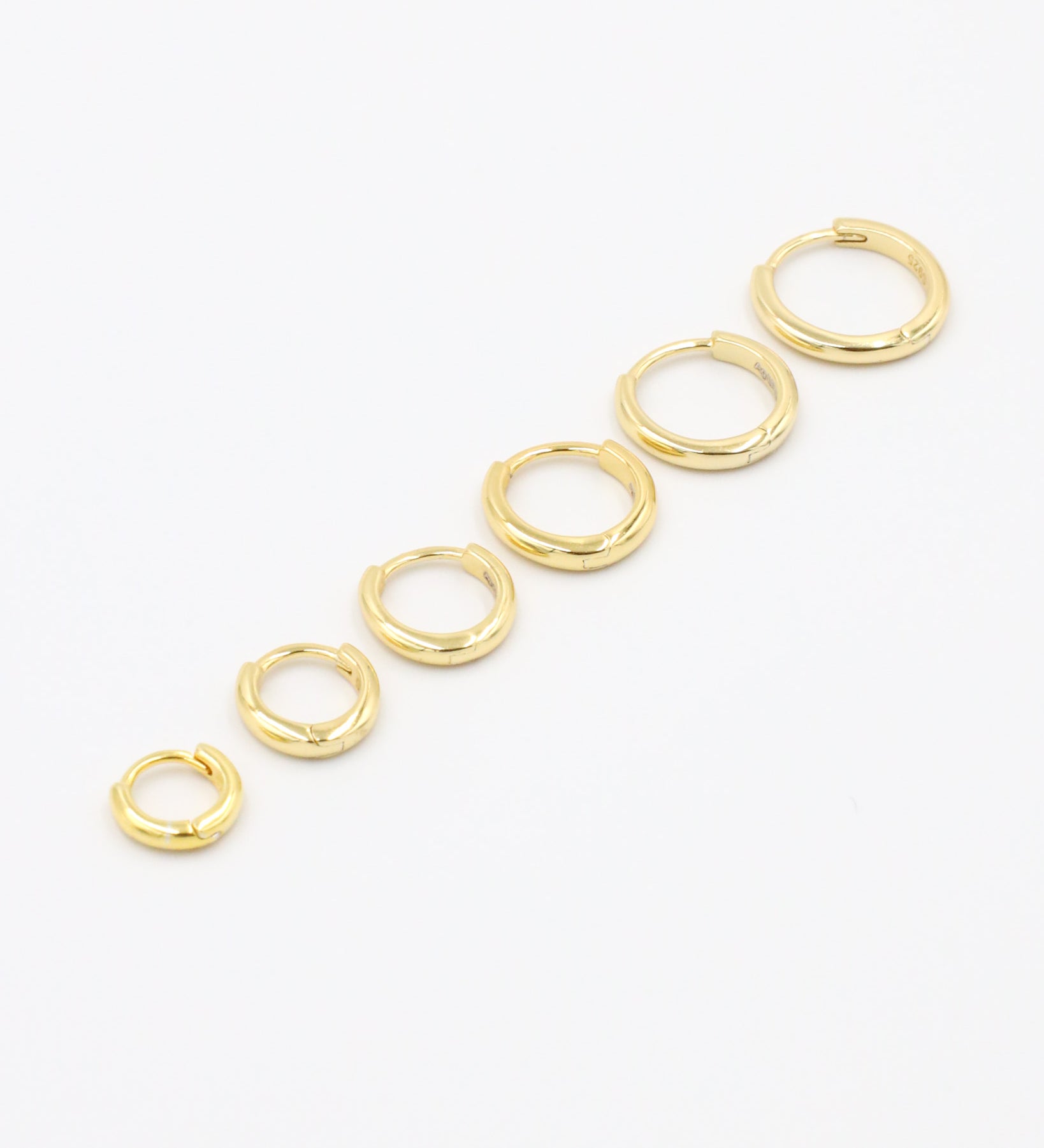 A series of circular gold colored hoops of varying sizes arranged in a line on a white background.
