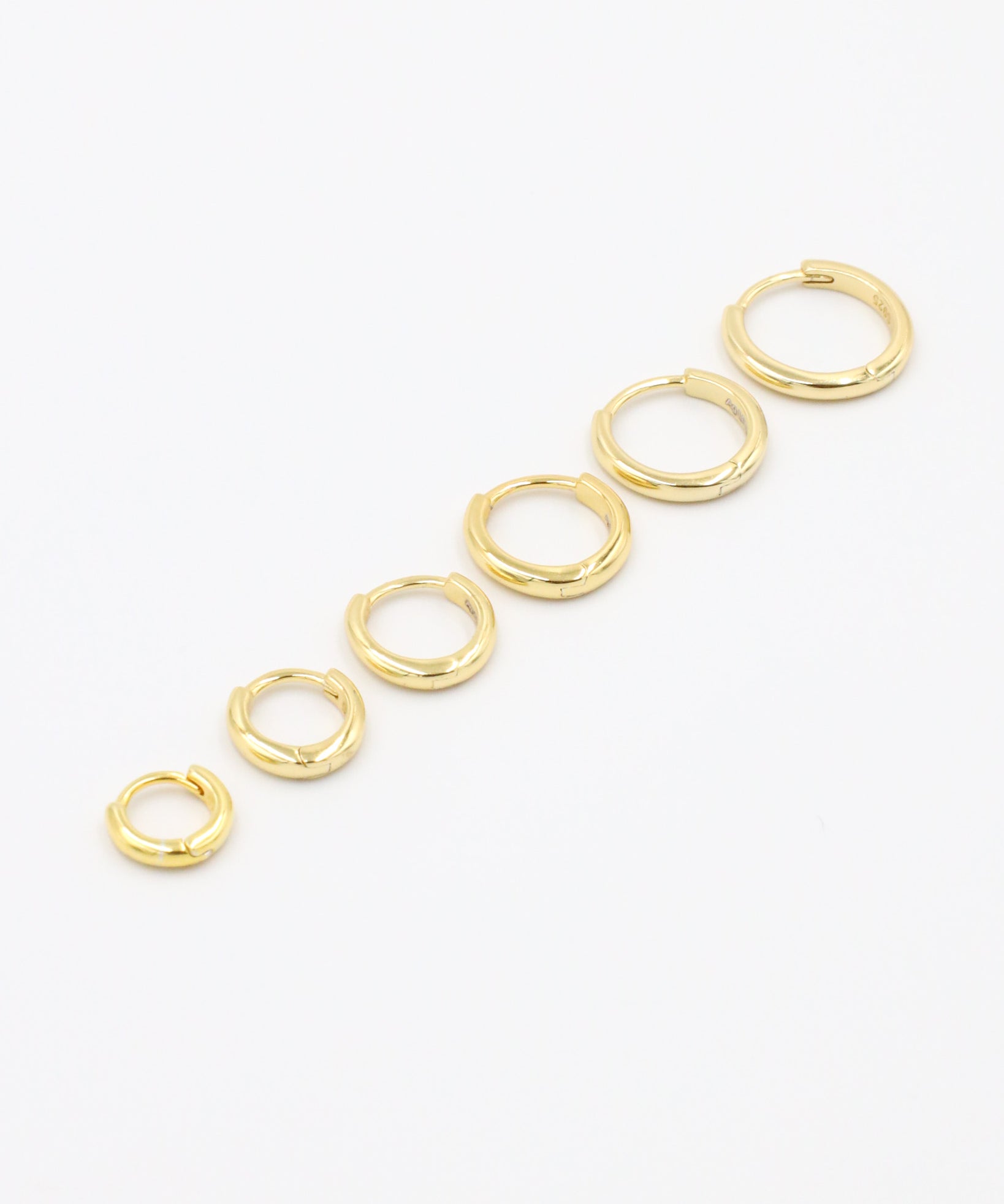 A series of circular gold colored hoops of varying sizes arranged in a line on a white background.