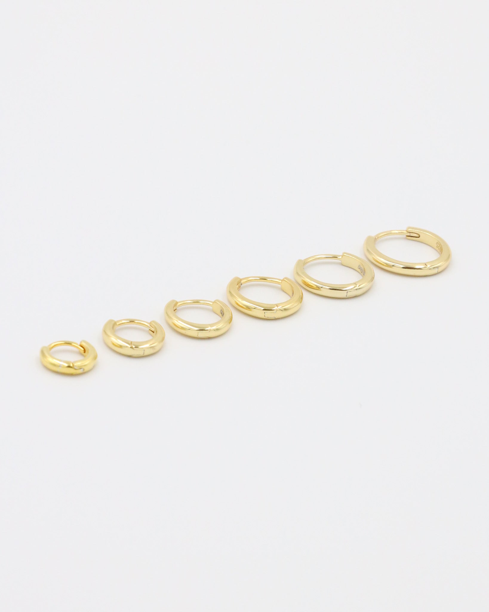 A series of circular gold colored hoops of varying sizes arranged in a line on a white background.