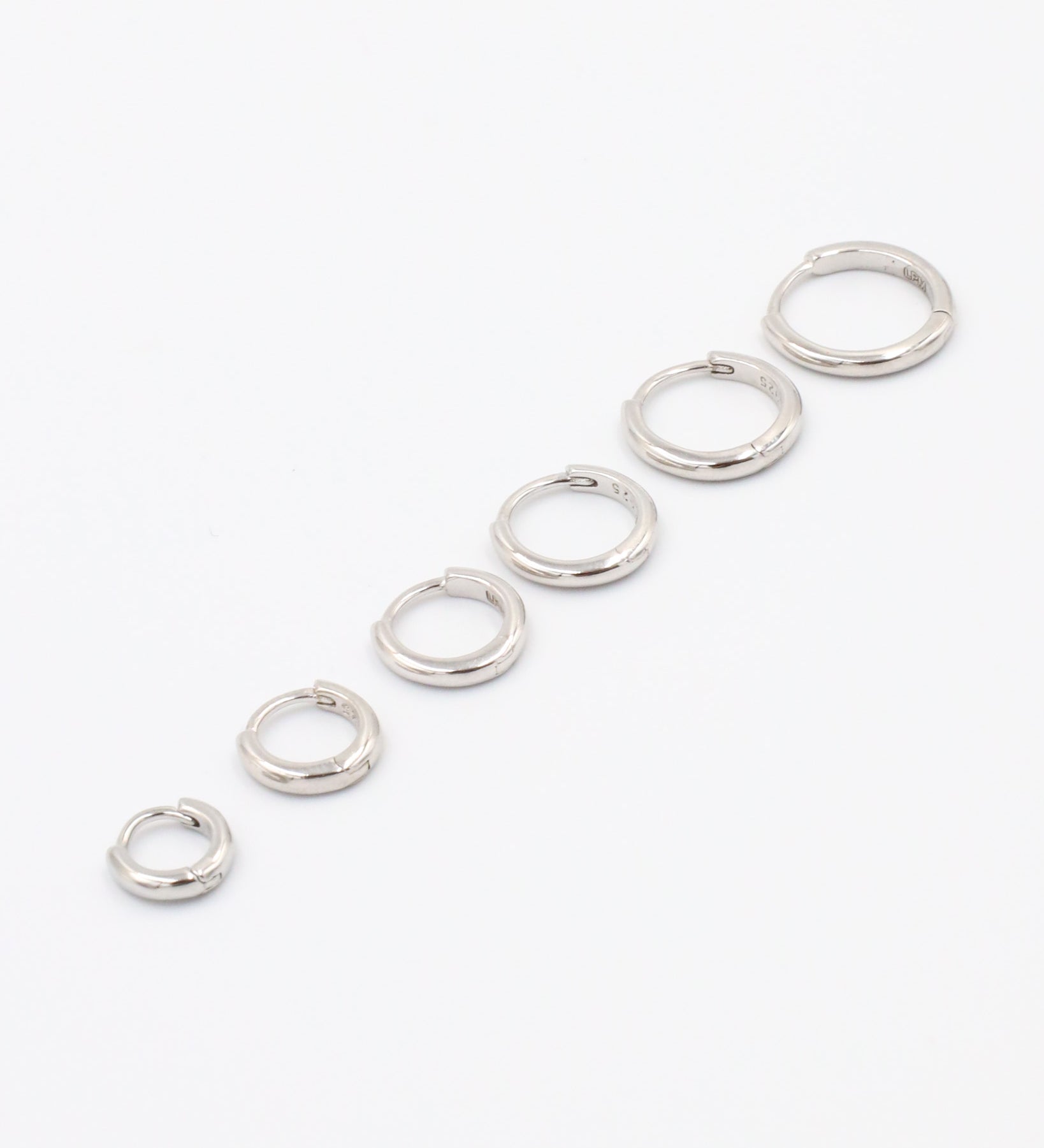 A series of circular silver colored hoops of varying sizes arranged in a line on a white background.