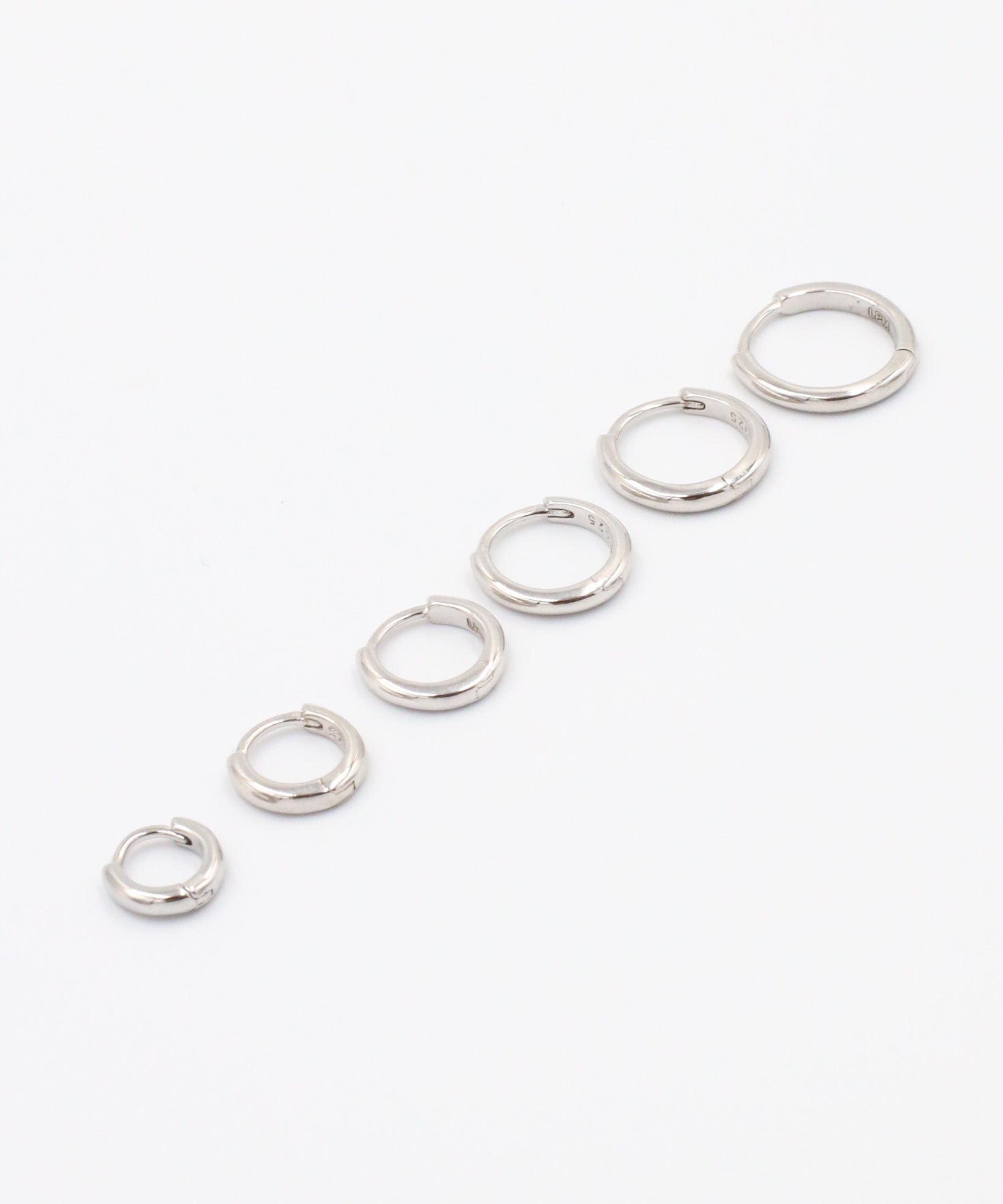 A series of circular silver colored hoops of varying sizes arranged in a line on a white background.