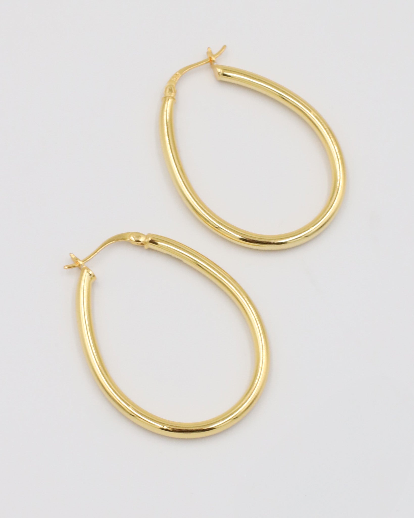 A pair of gold creole earrings with a latch back clasp on a white background.