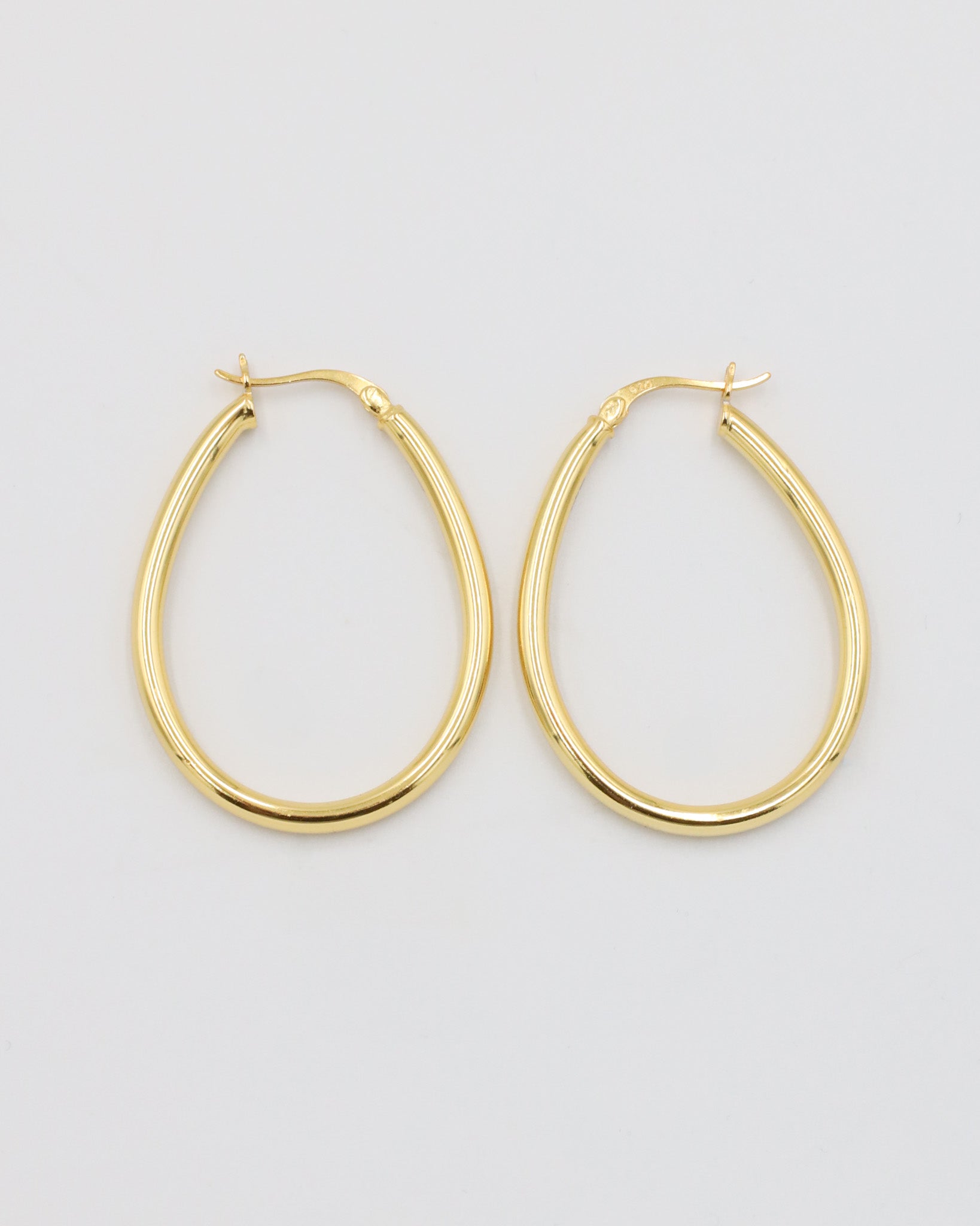 A pair of gold creole earrings with a latch back clasp on a white background.