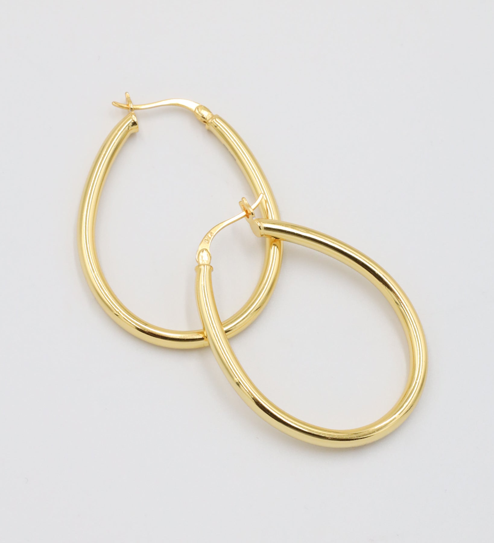 A pair of gold creole earrings with a latch back clasp on a white background.