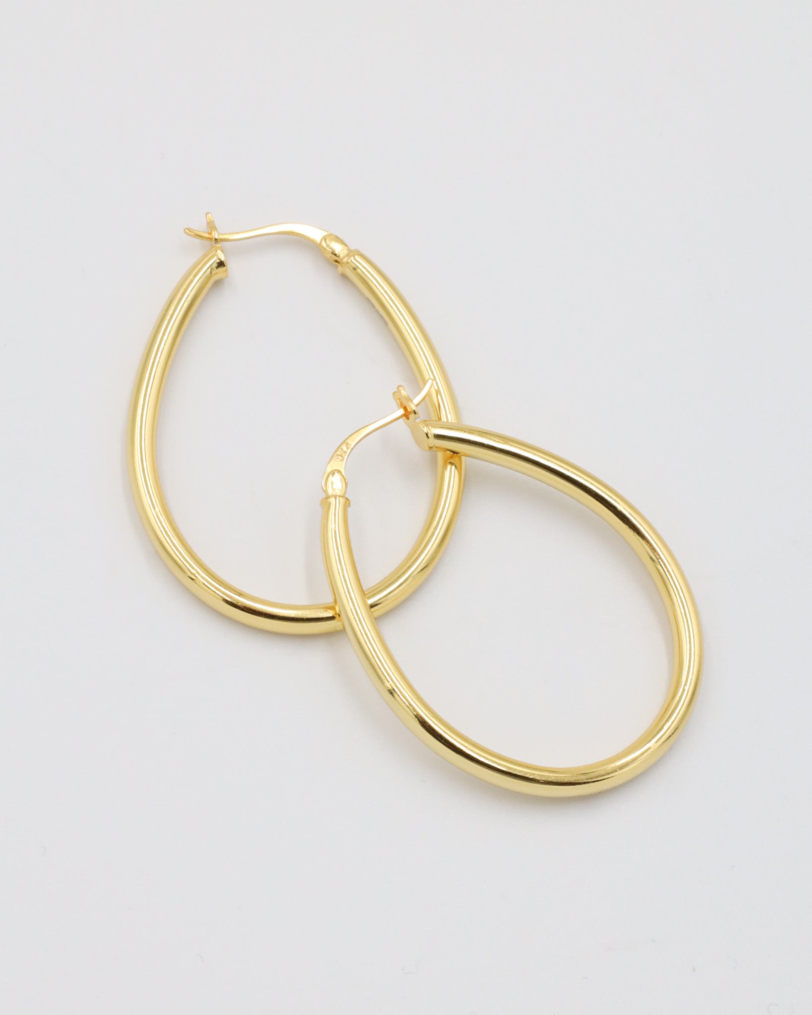 A pair of gold creole earrings with a latch back clasp on a white background.