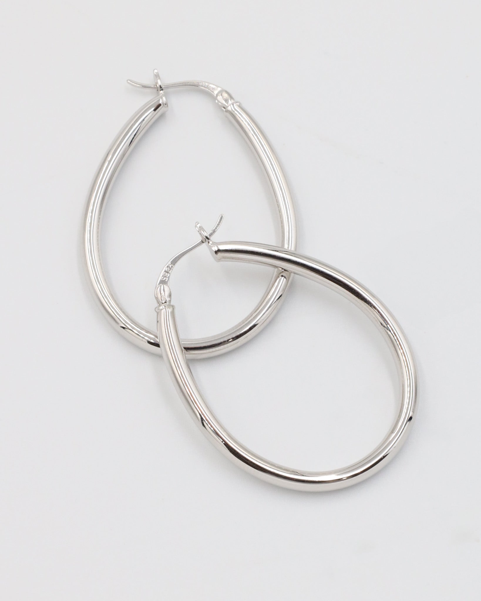A pair of silver creole earrings with a latch back clasp on a white background.