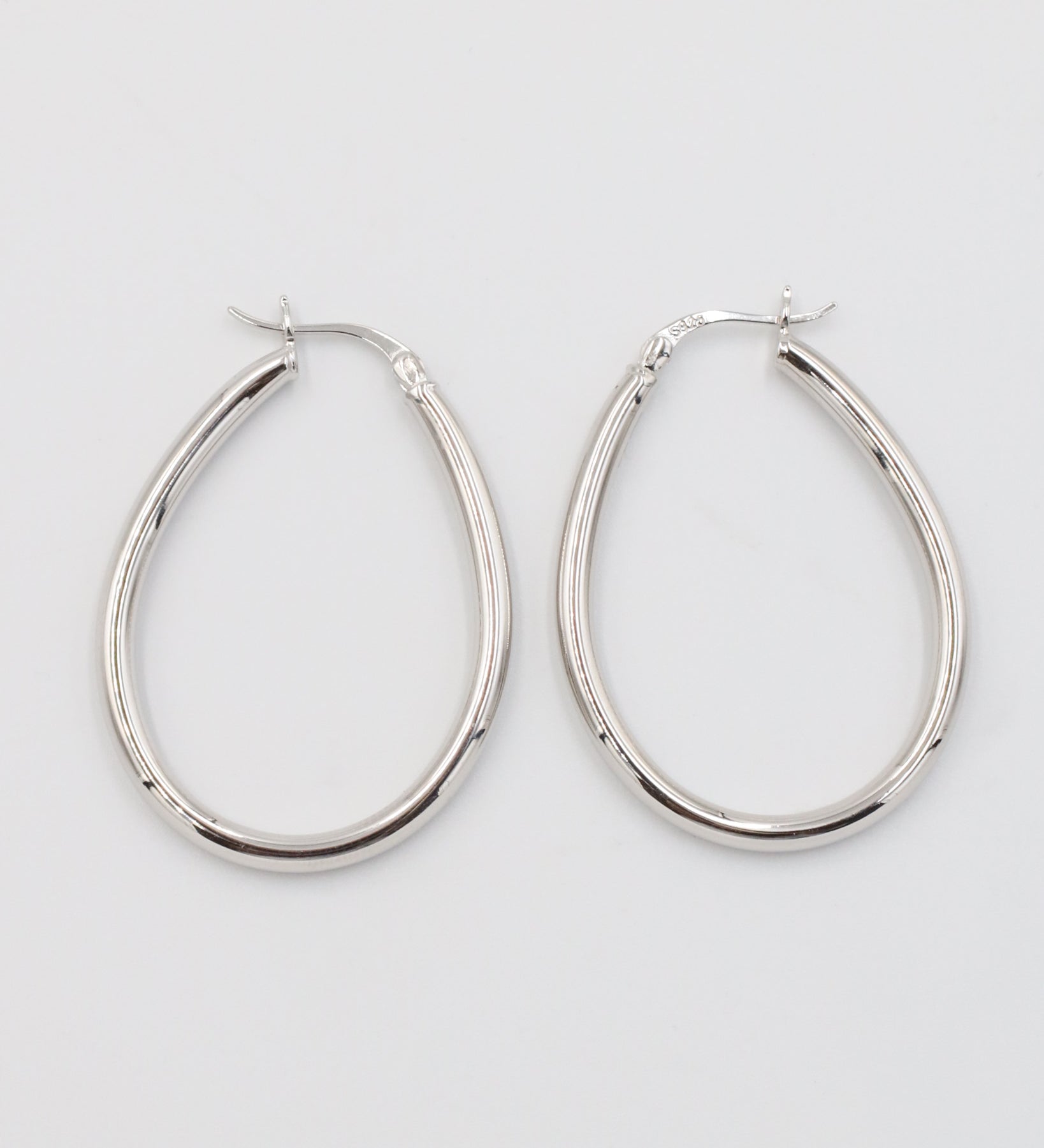 A pair of silver creole earrings with a latch back clasp on a white background.