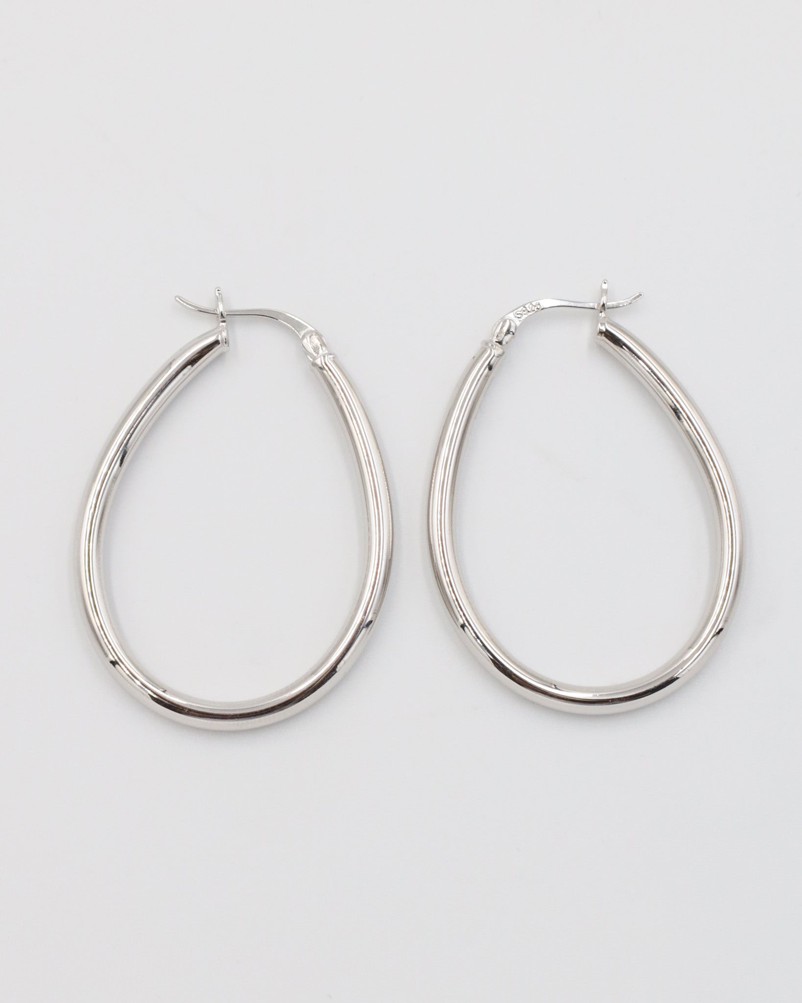A pair of silver creole earrings with a latch back clasp on a white background.