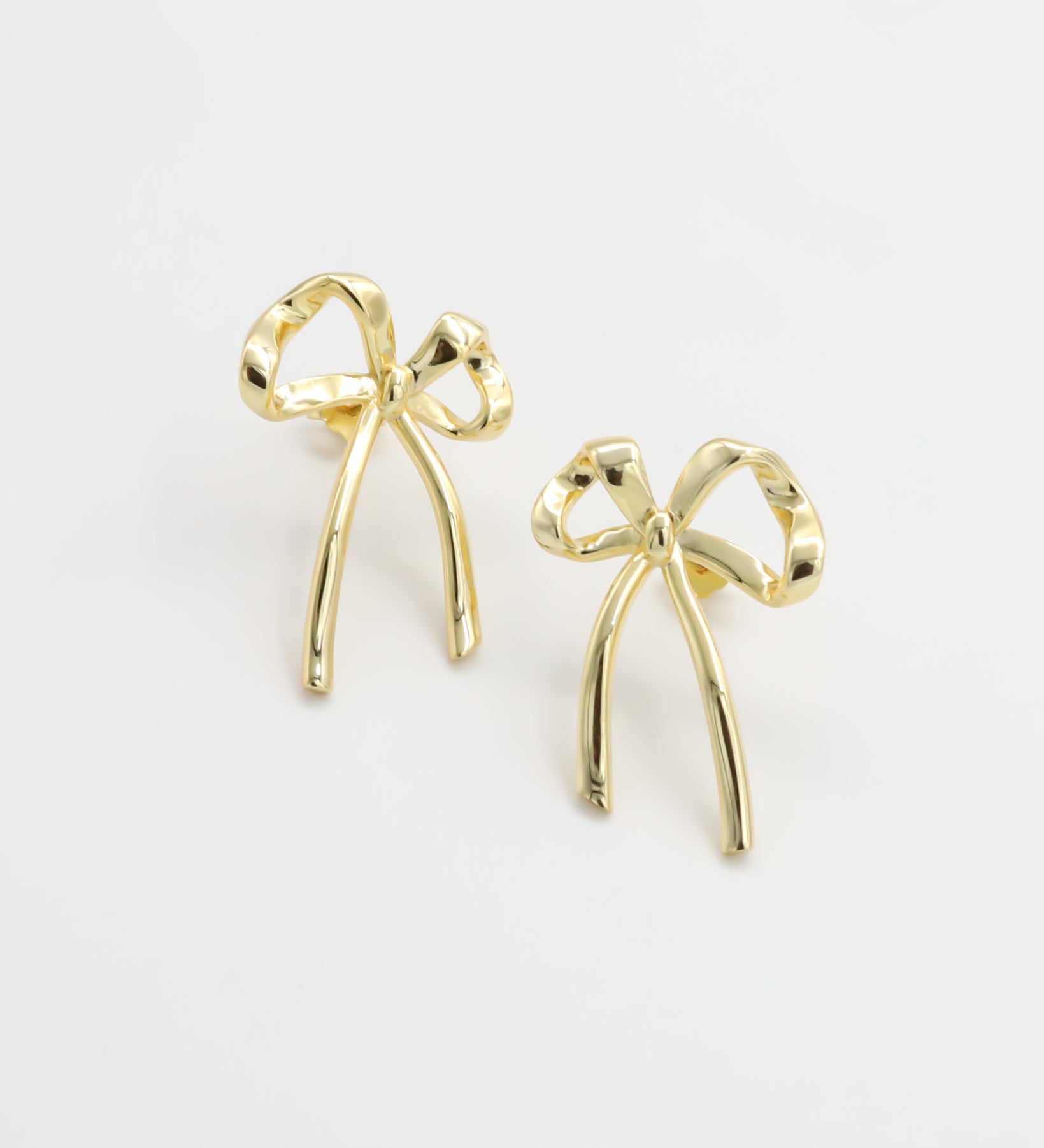 A pair of gold-colored ribbon-shaped stud earrings on a white background