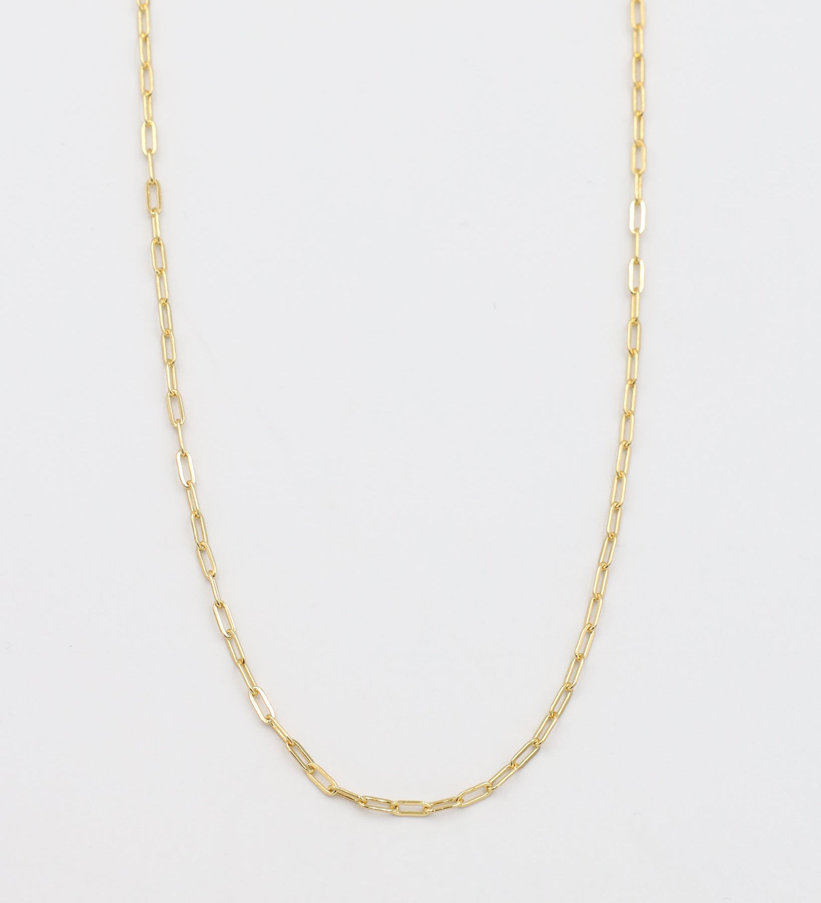 A gold-colored necklace with a chain link design, laid out on a plain background.
