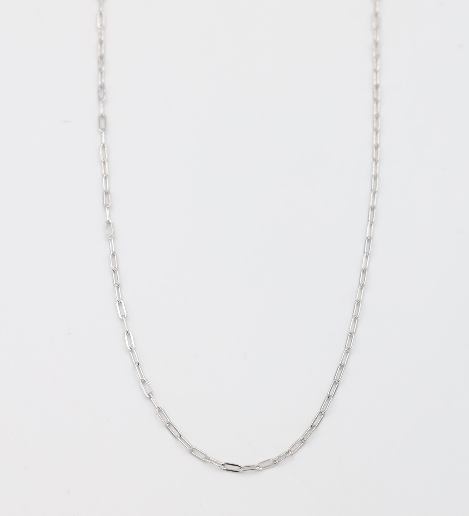 A silver necklace with a chain link design, laid out on a plain background.