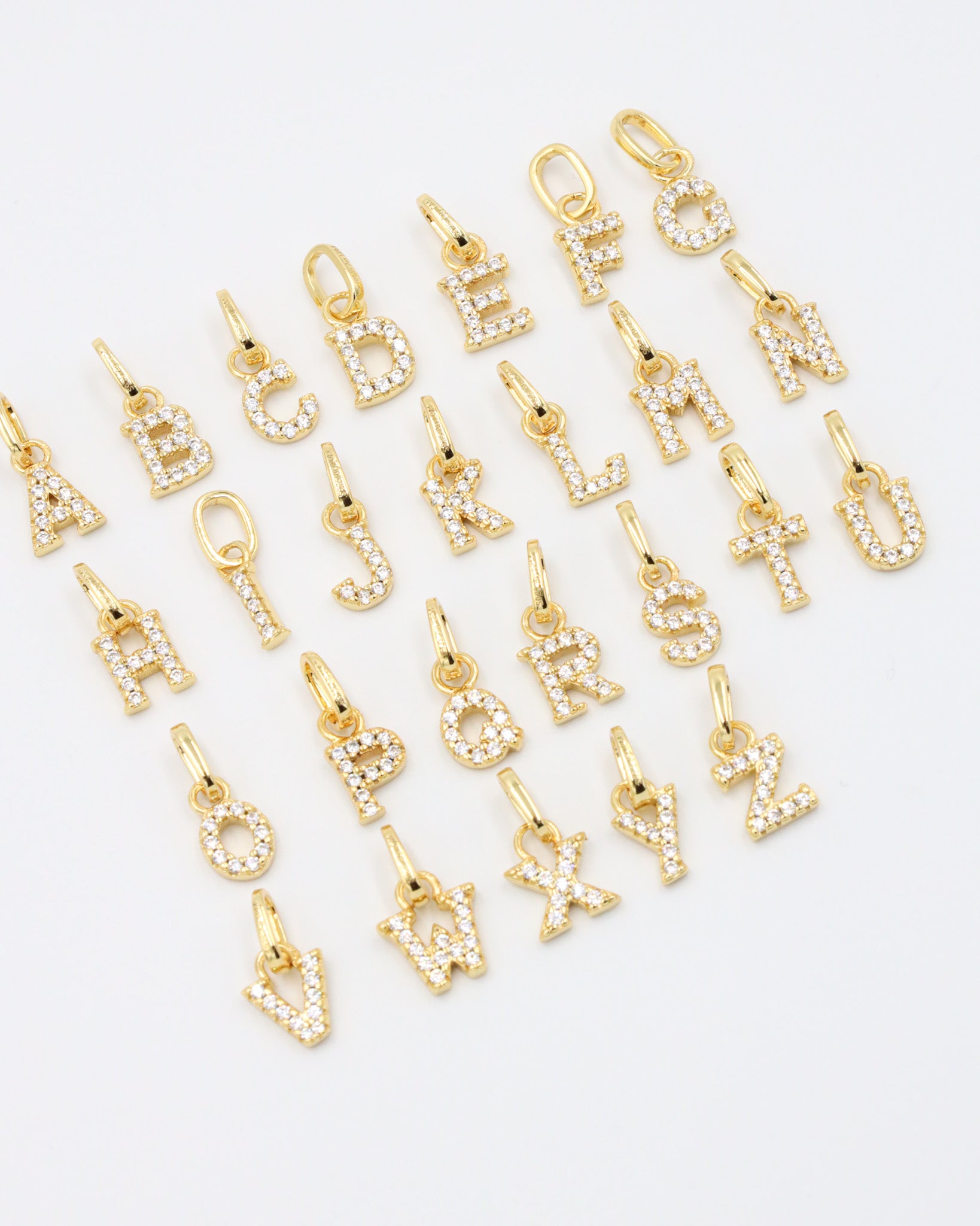 Gold-plated letter pendants in an A-Z arrangement, captured at an angle to highlight their sparkling zirconia stones.