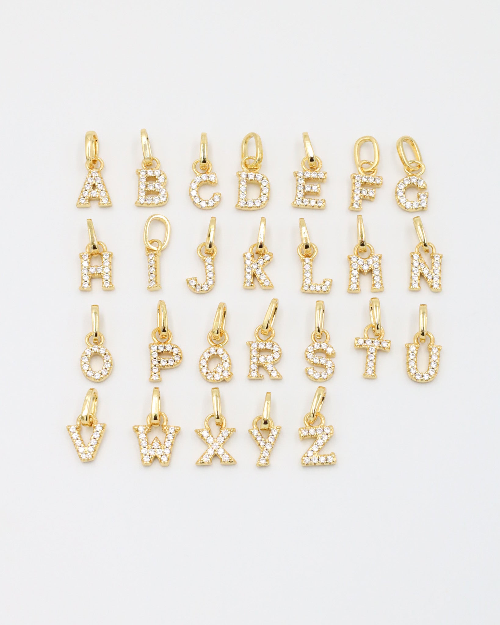 Gold-plated sparkly letter pendants arranged in a complete A-Z display, showcasing their zirconia embellishments.