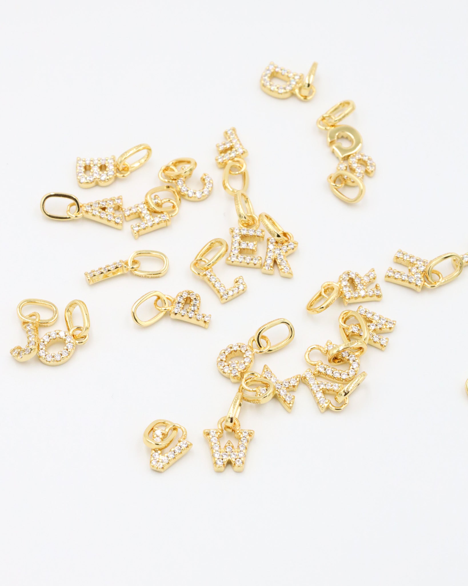 Scattered gold-plated letter pendants, each adorned with sparkling zirconia stones, perfect for a personalized look.