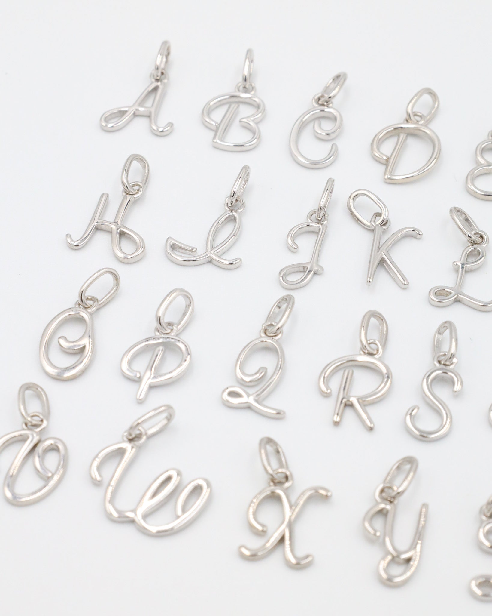 Close-up of rhodium plated 925 sterling silver letter curve pendants, showcasing details of the individual letters.