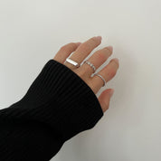 A silver ring with a twisted band design worn by a hand with a black sweater.