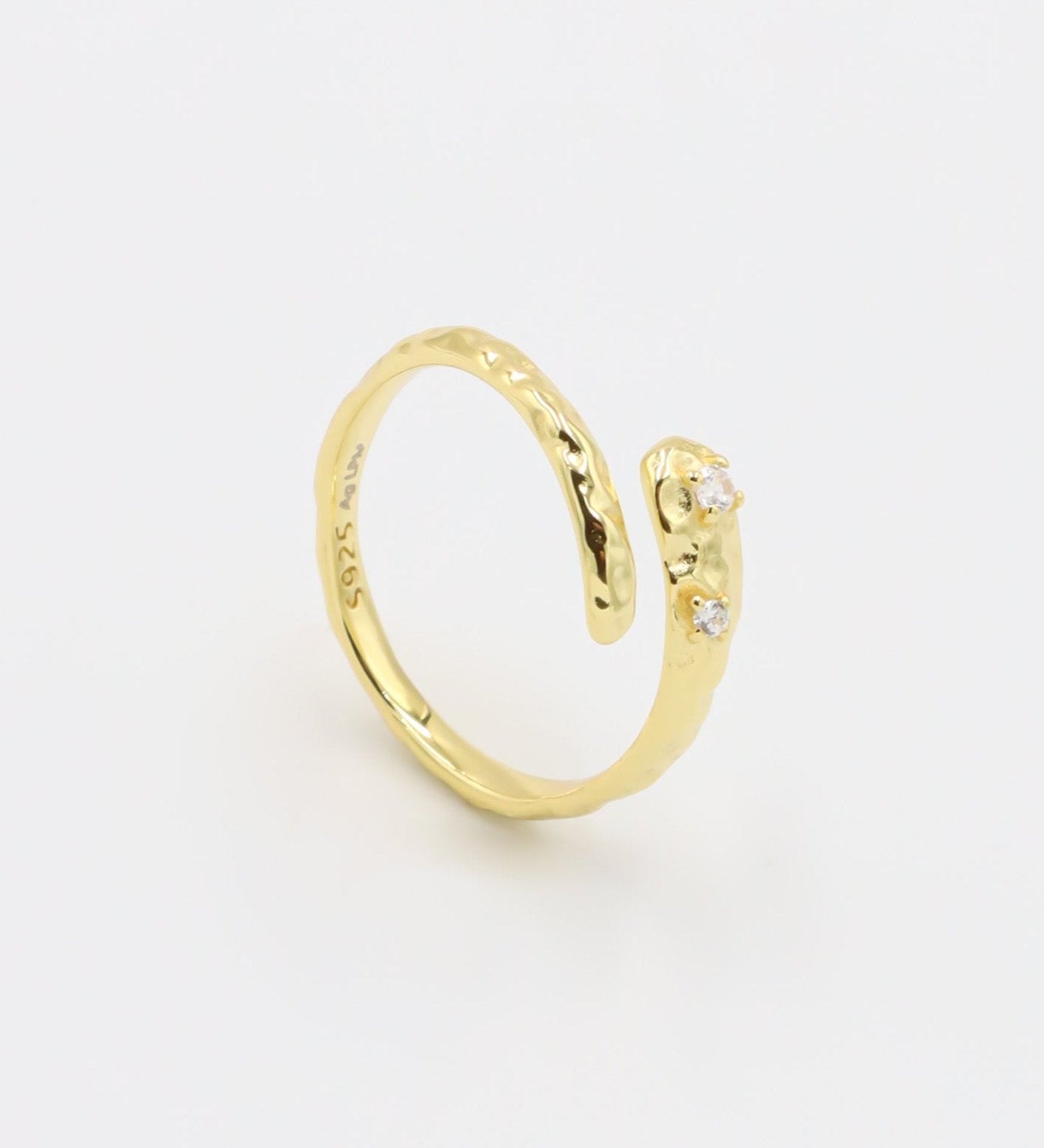 Close-up of an open gold-plated 925 sterling silver ring with a hammered texture and three delicate zirconia stones, handcrafted and photographed on a white background – minimalist Swiss jewelry design.