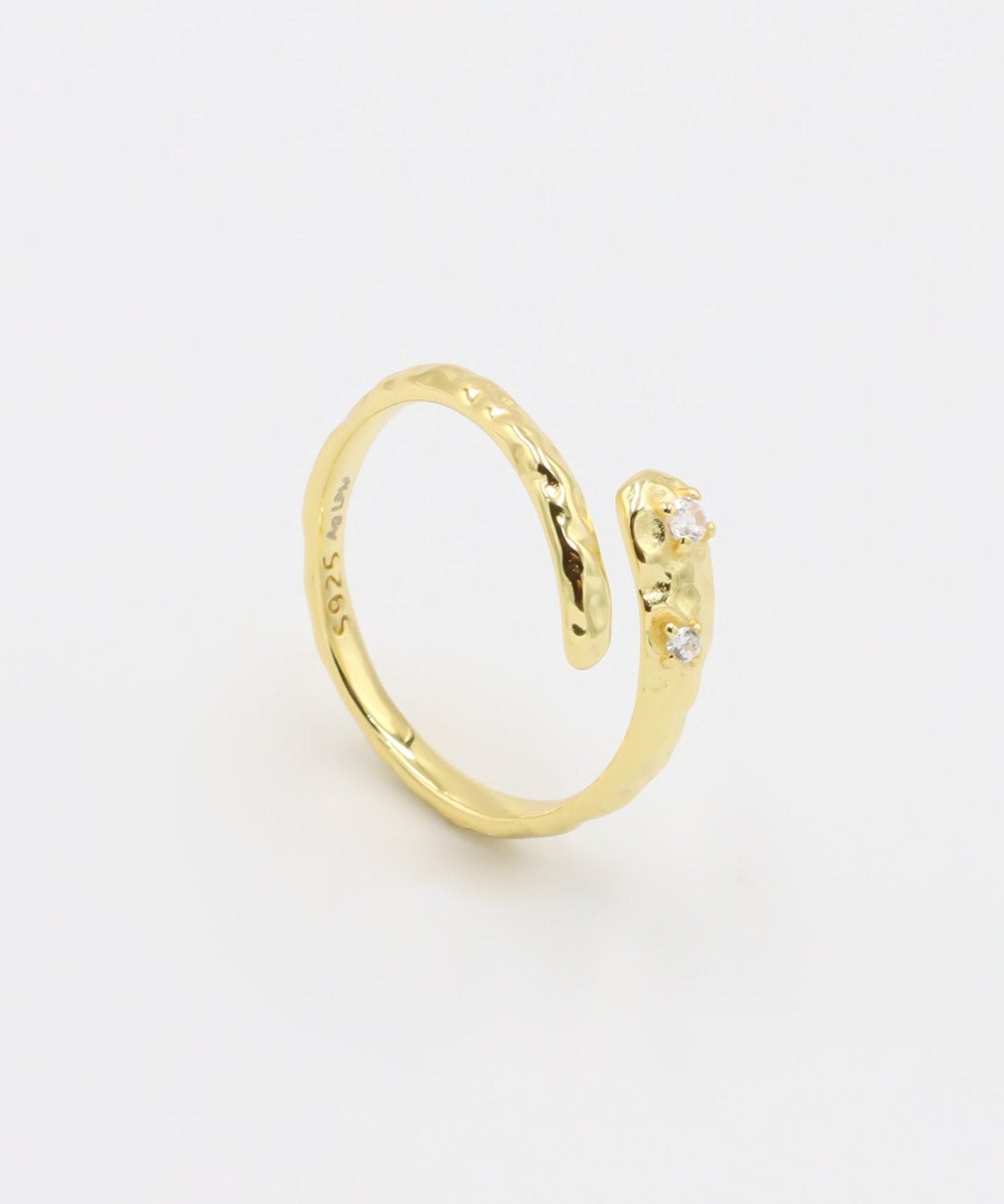 Close-up of an open gold-plated 925 sterling silver ring with a hammered texture and three delicate zirconia stones, handcrafted and photographed on a white background – minimalist Swiss jewelry design.