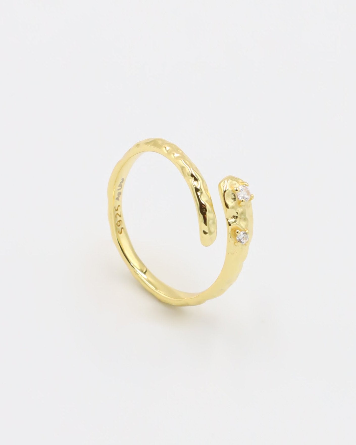 Close-up of an open gold-plated 925 sterling silver ring with a hammered texture and three delicate zirconia stones, handcrafted and photographed on a white background – minimalist Swiss jewelry design.