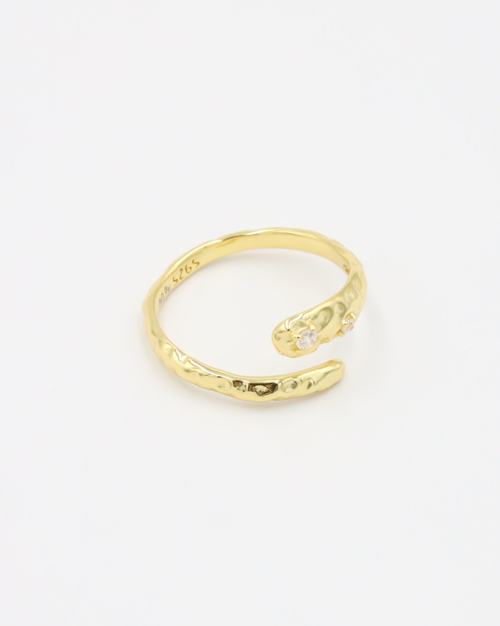 Close-up of an open gold-plated 925 sterling silver ring with a hammered texture and three delicate zirconia stones, handcrafted and photographed on a white background – minimalist Swiss jewelry design.
