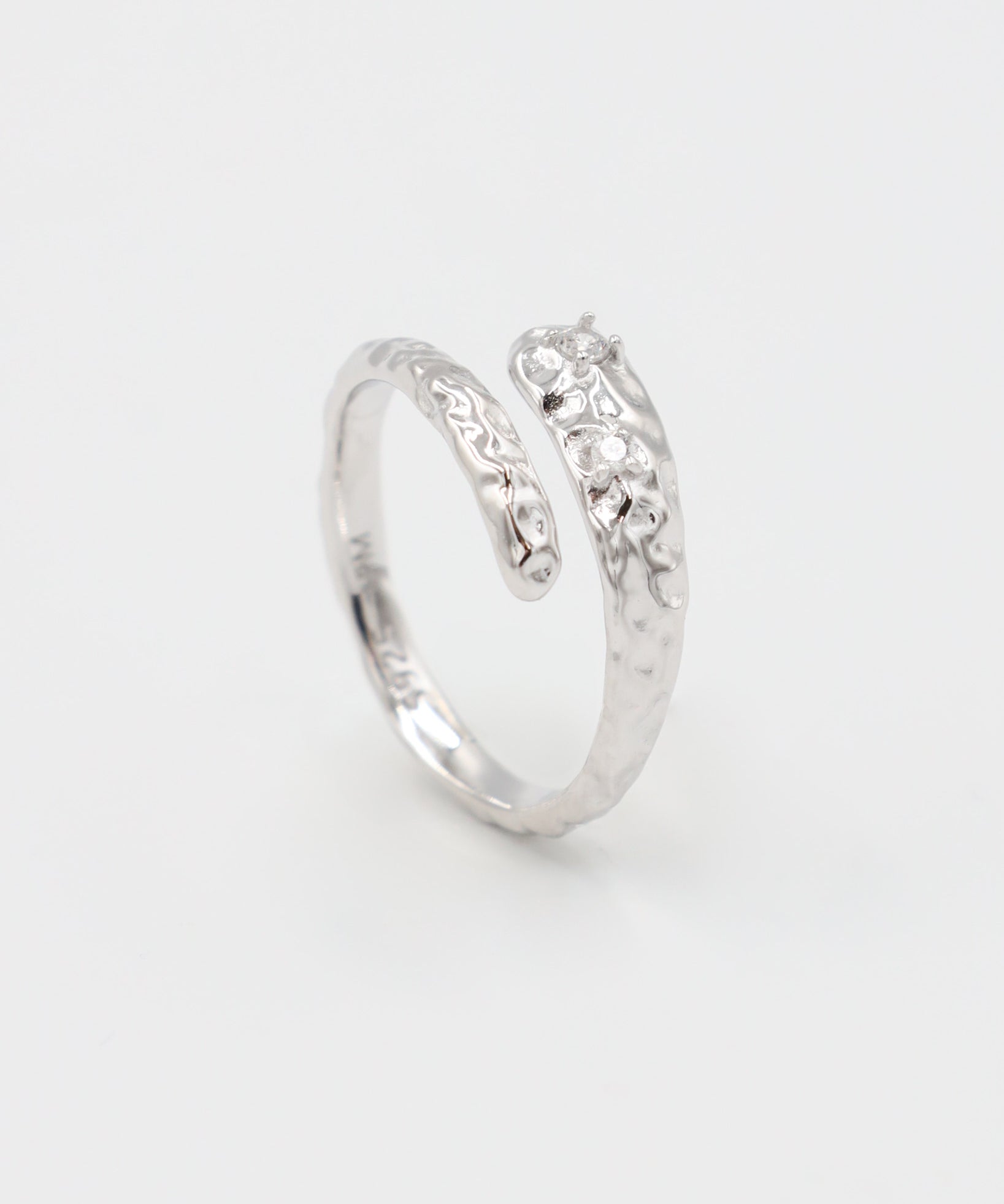 Close-up of an open rhodium-plated 925 sterling silver ring with a hammered texture and three delicate zirconia stones, handcrafted and photographed on a white background – minimalist Swiss jewelry design.