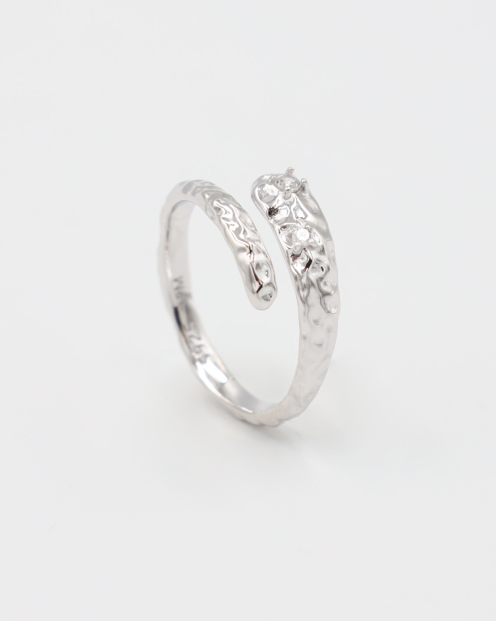 Close-up of an open rhodium-plated 925 sterling silver ring with a hammered texture and three delicate zirconia stones, handcrafted and photographed on a white background – minimalist Swiss jewelry design.