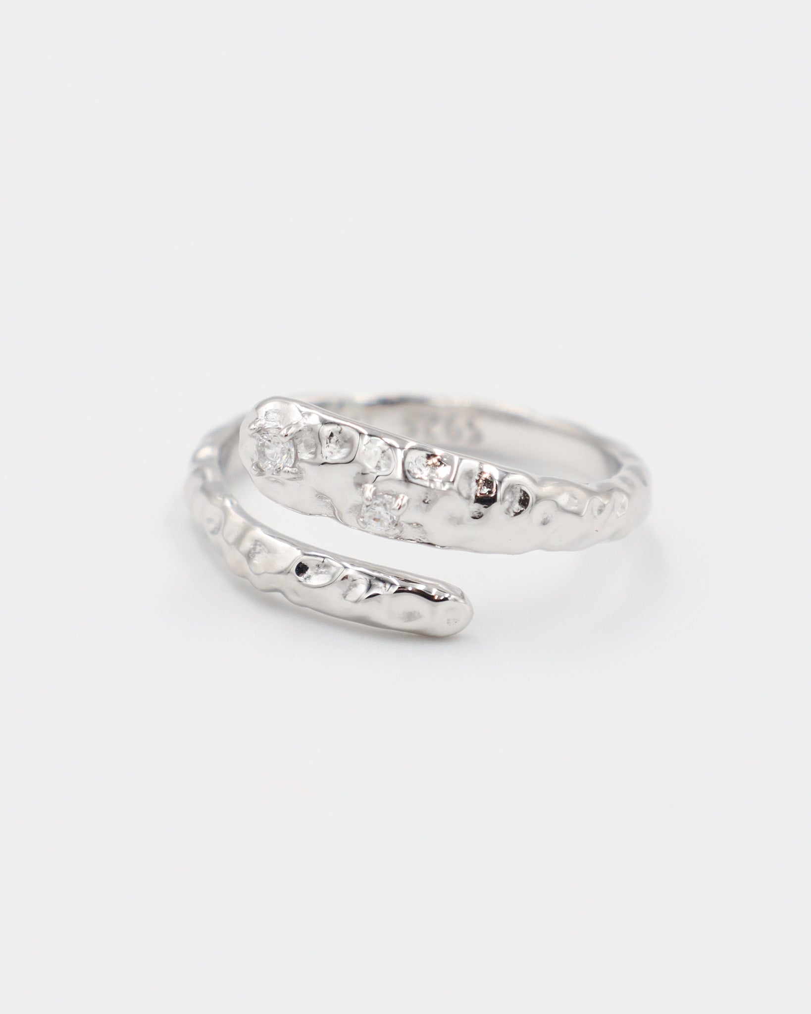 Close-up of an open rhodium-plated 925 sterling silver ring with a hammered texture and three delicate zirconia stones, handcrafted and photographed on a white background – minimalist Swiss jewelry design.