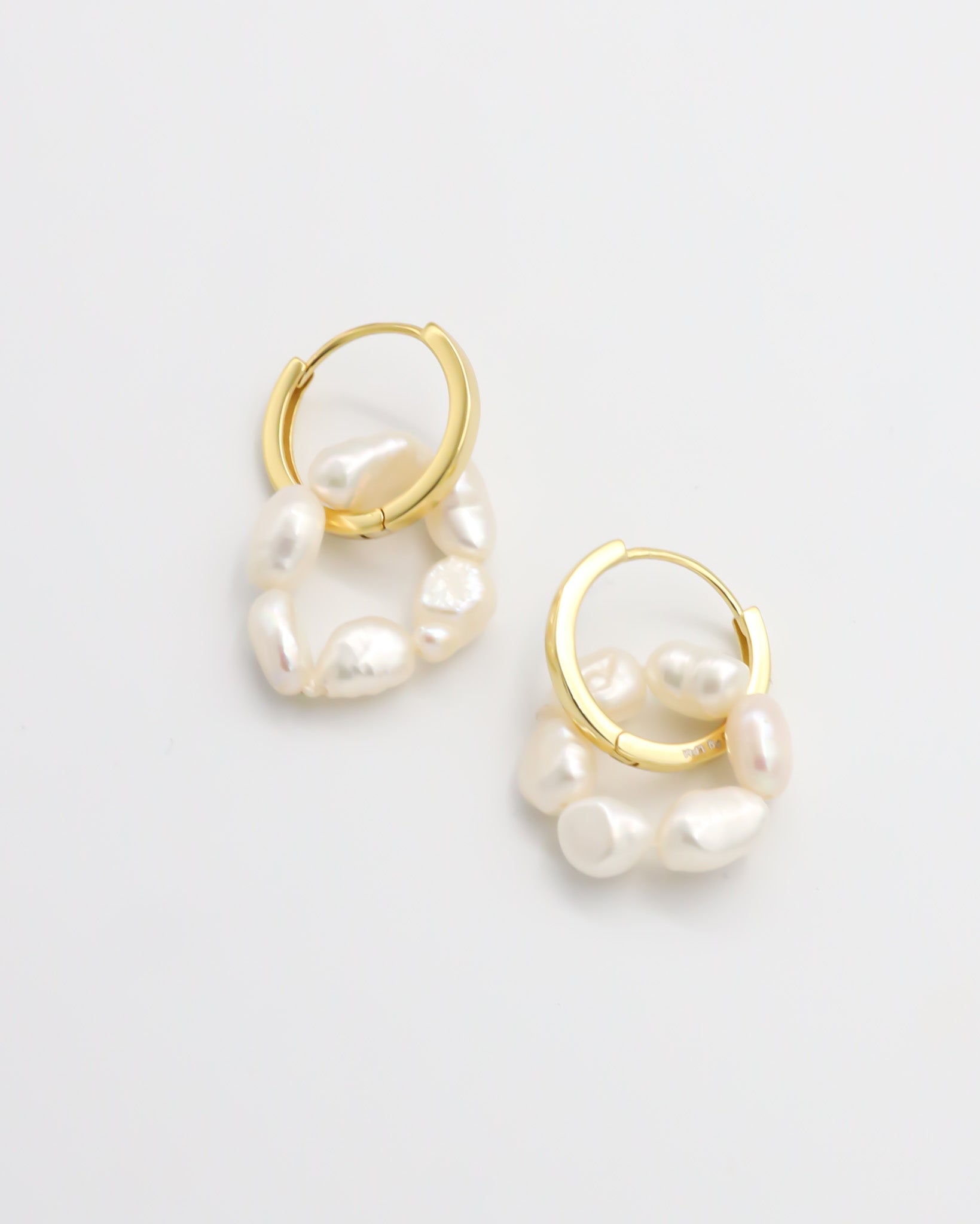 A pair of gold hoop earrings with white pearls attached to them, displayed on a white background.