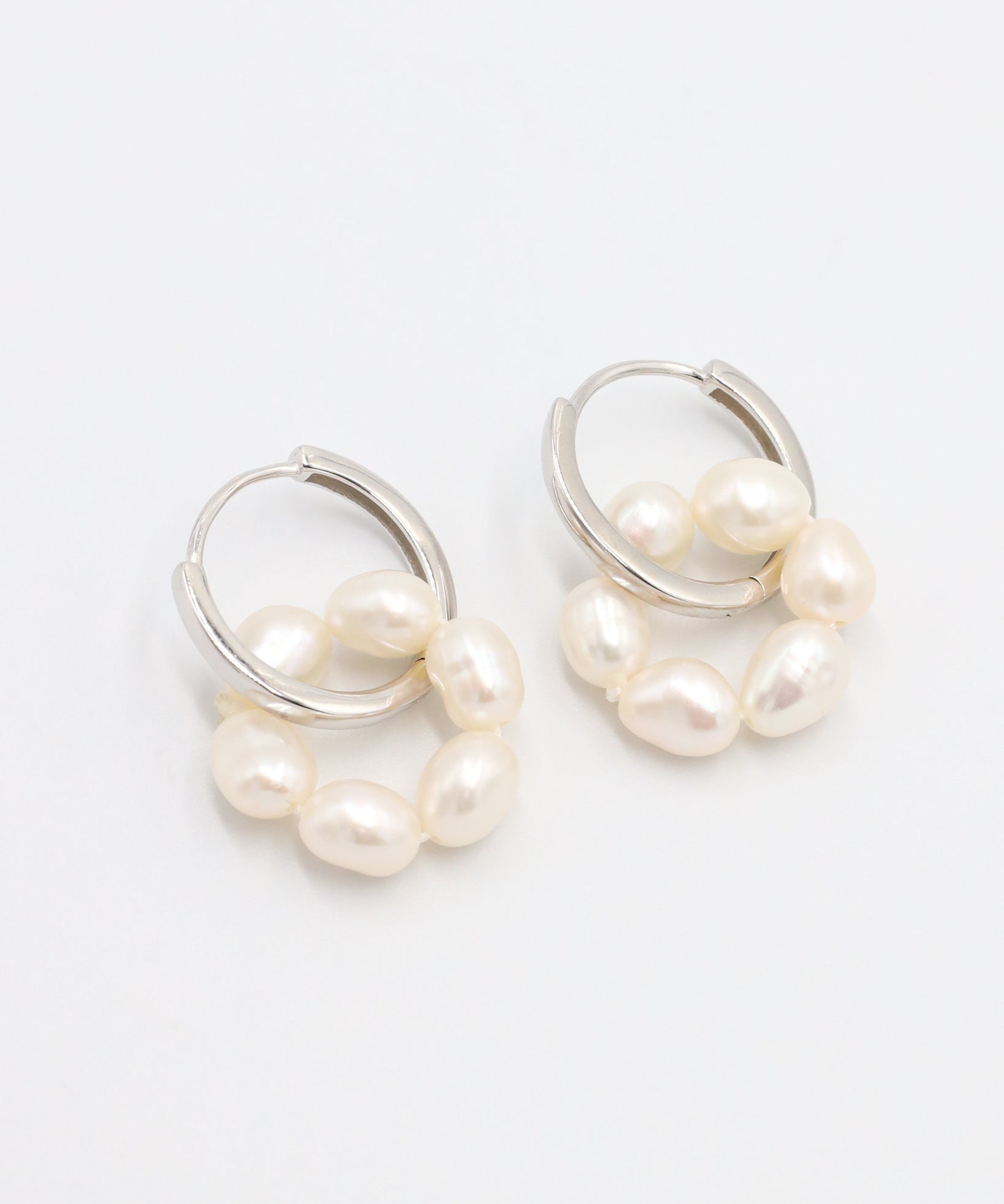 A pair of silver hoop earrings with white pearls attached to them, displayed on a white background.