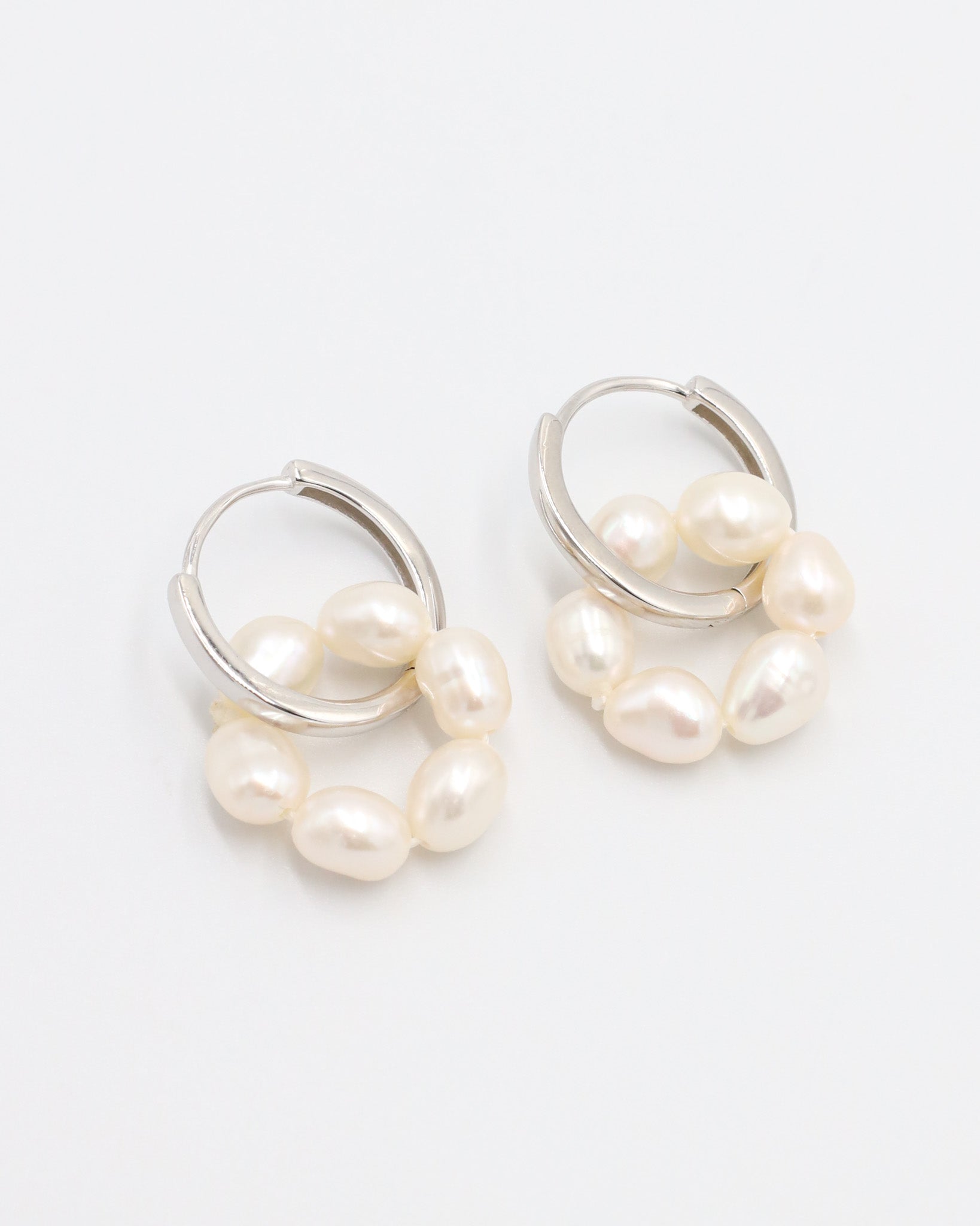A pair of silver hoop earrings with white pearls attached to them, displayed on a white background.