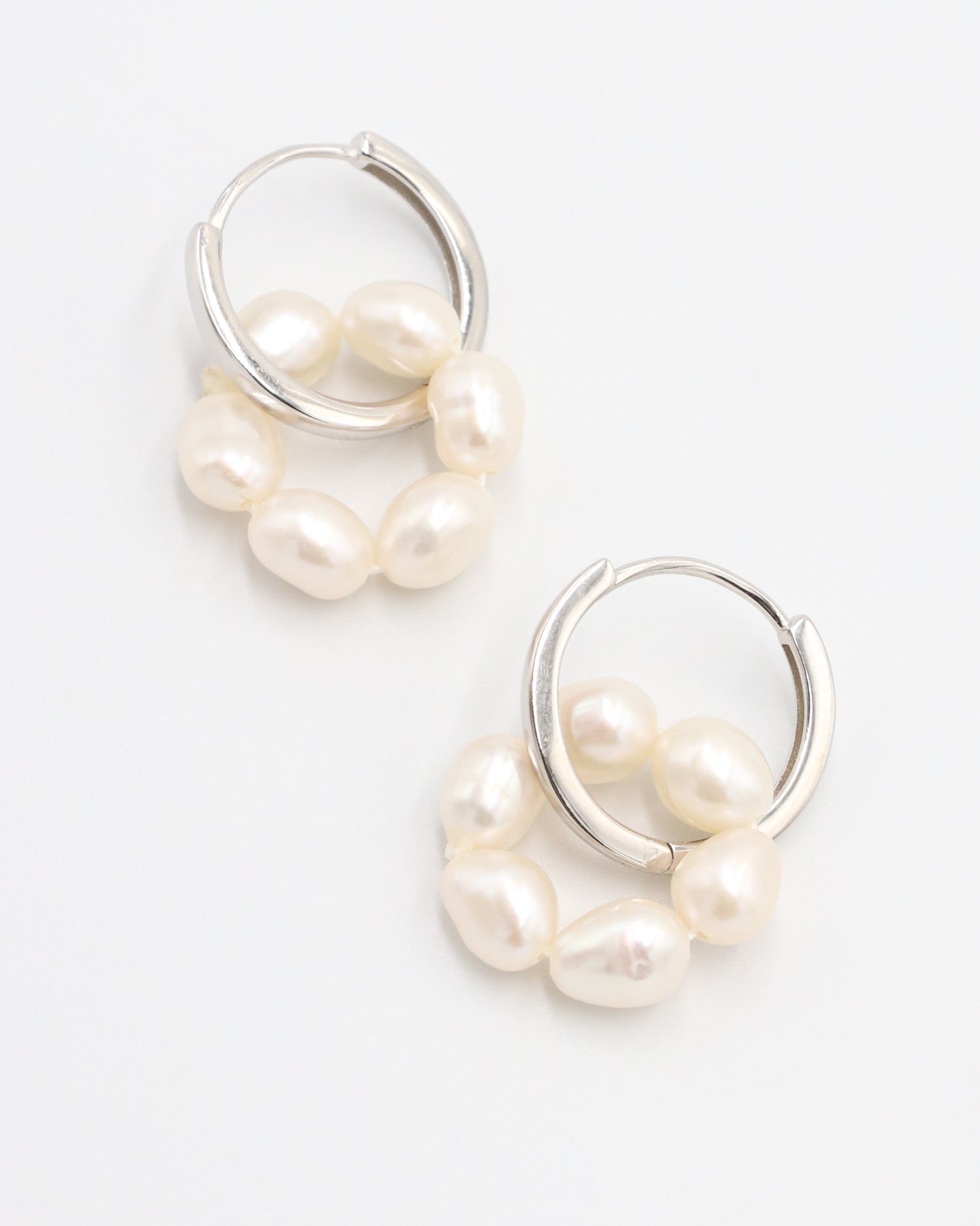 A pair of silver hoop earrings with white pearls attached to them, displayed against a white background.