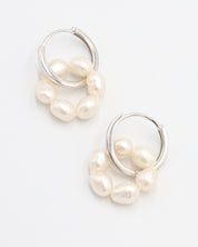 A pair of silver hoop earrings with white pearls attached to them, displayed against a white background.