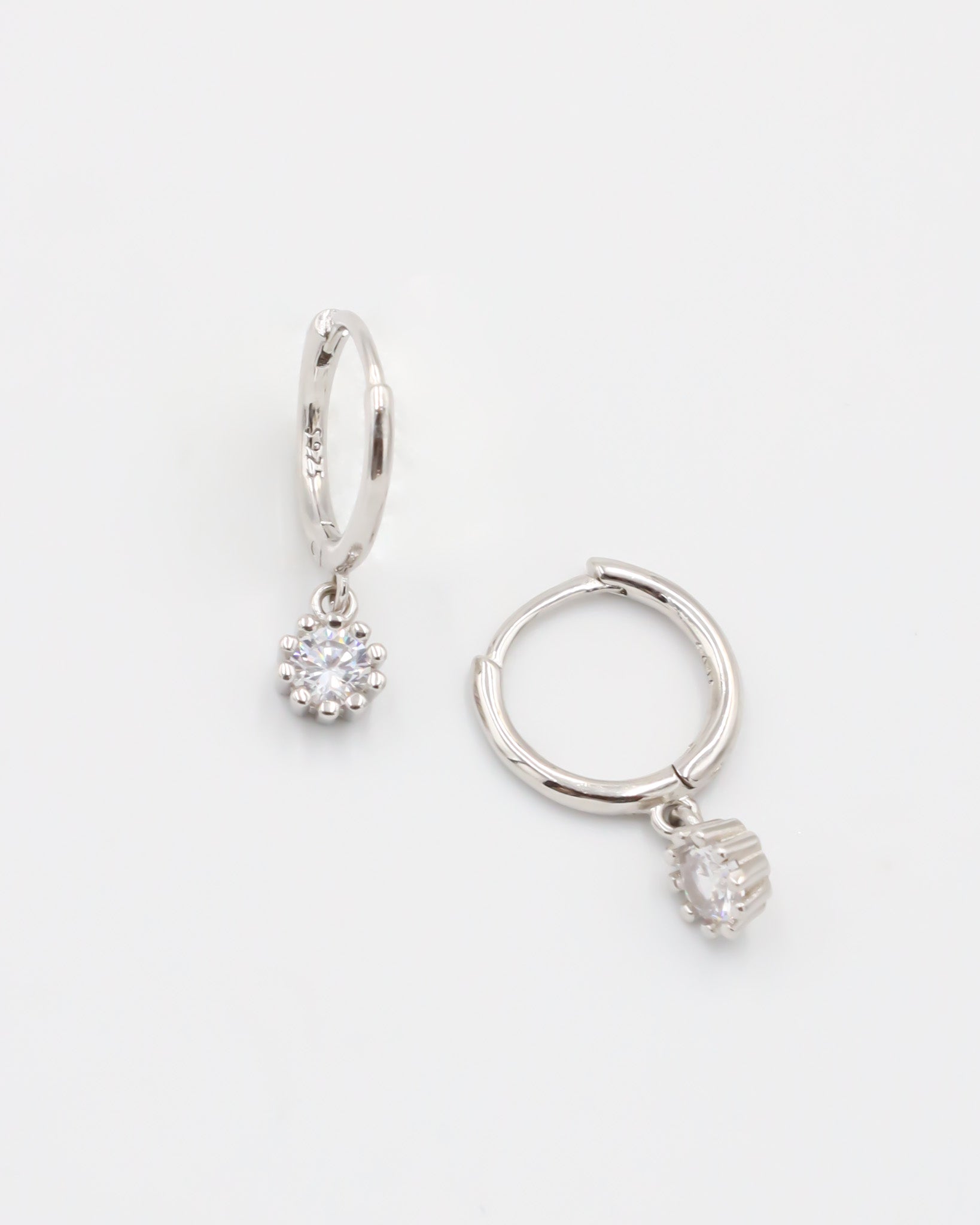 A silver hoop earring with a hinged clasp and a dangling clear crystal-like pendant.