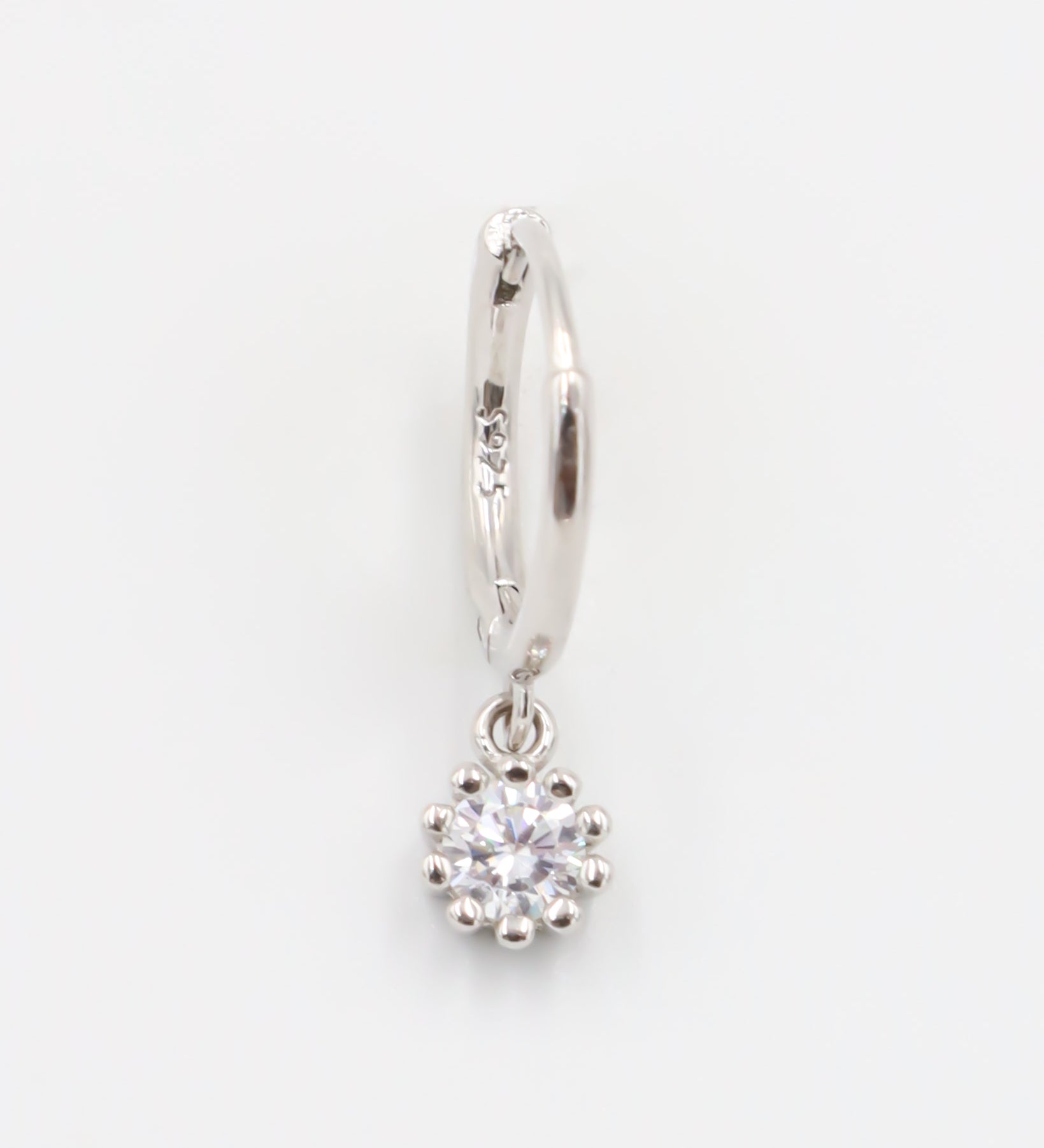 A silver hoop earring with a hinged clasp and a dangling clear crystal-like pendant.