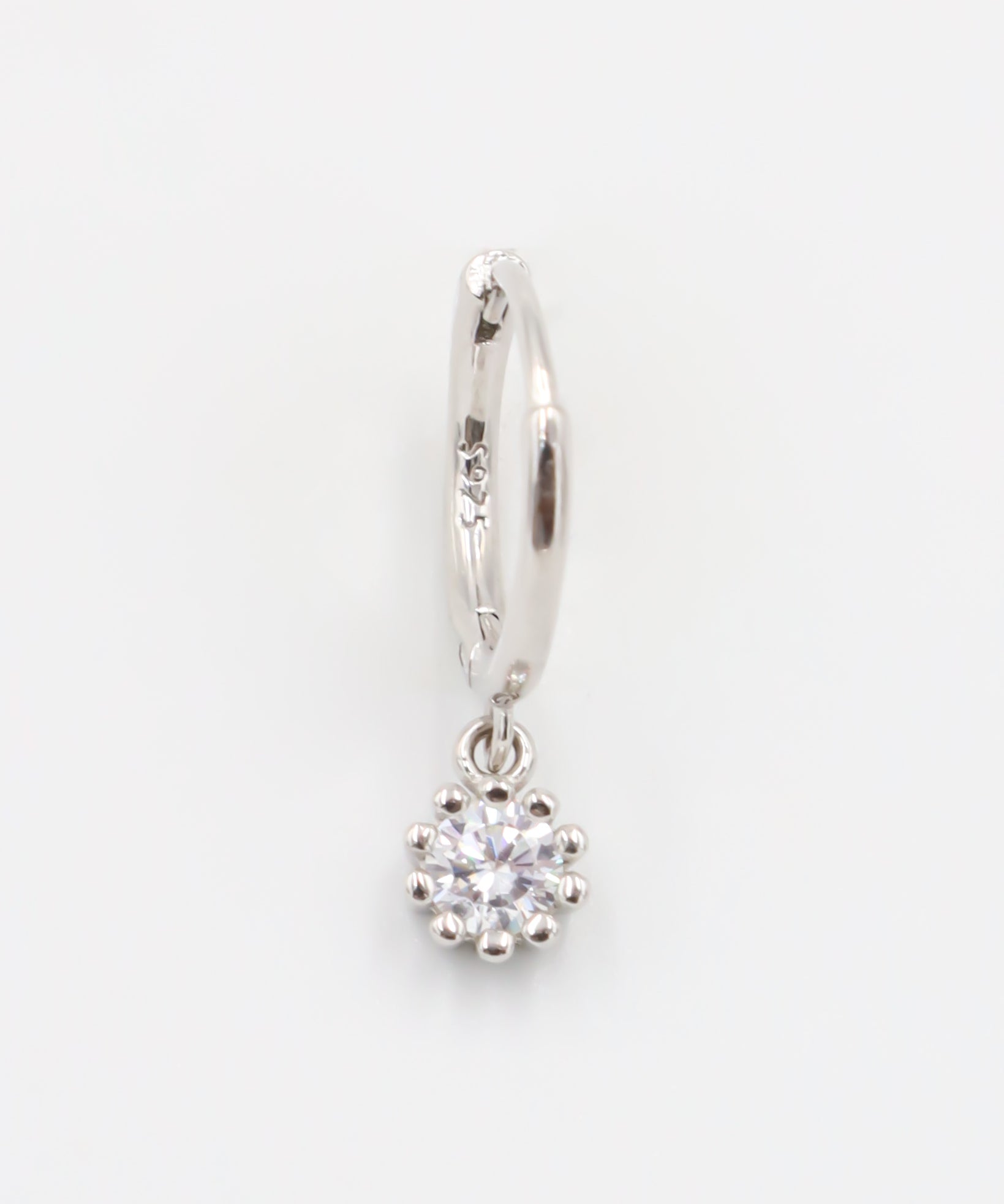 A silver hoop earring with a hinged clasp and a dangling clear crystal-like pendant.