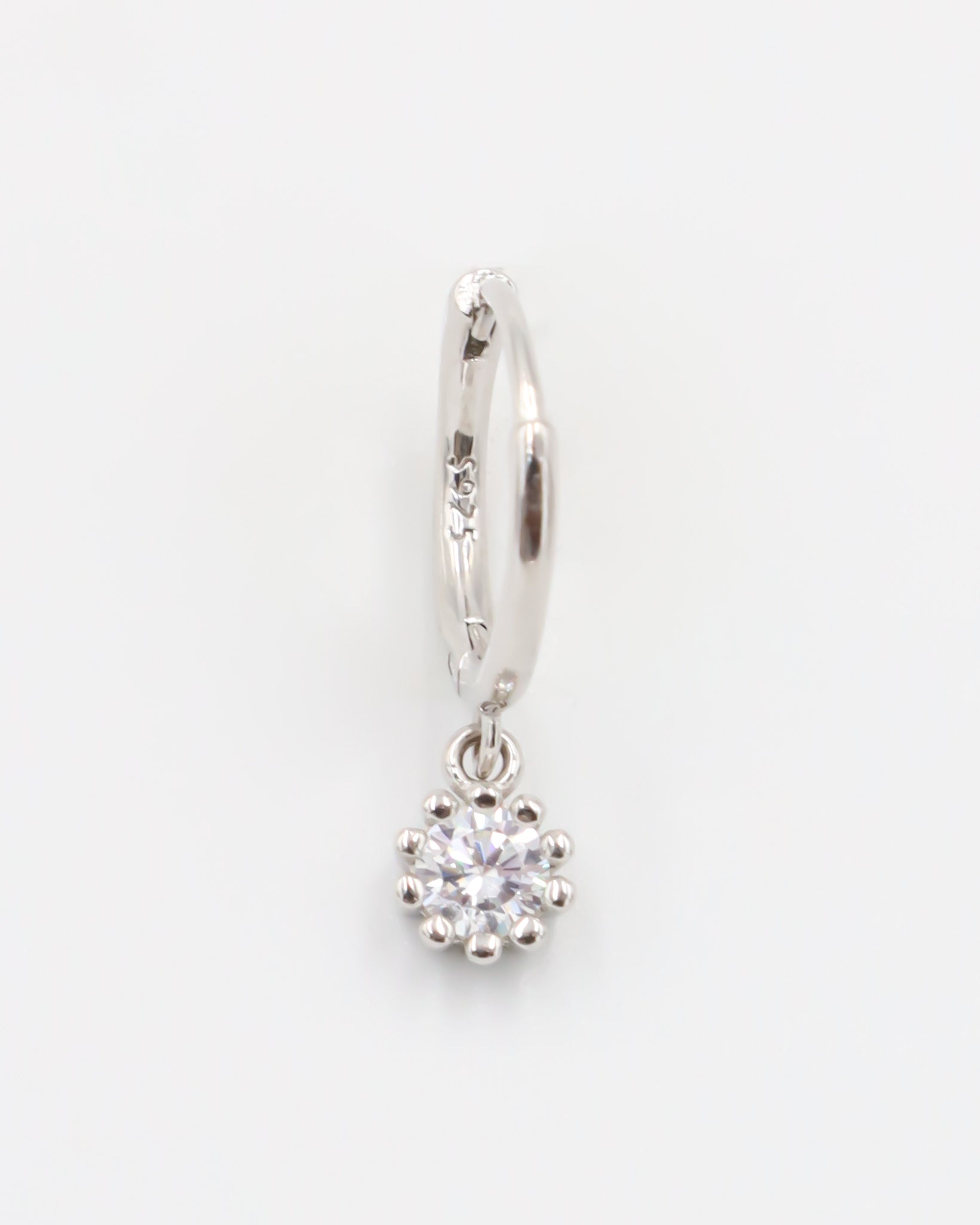 A silver hoop earring with a hinged clasp and a dangling clear crystal-like pendant.