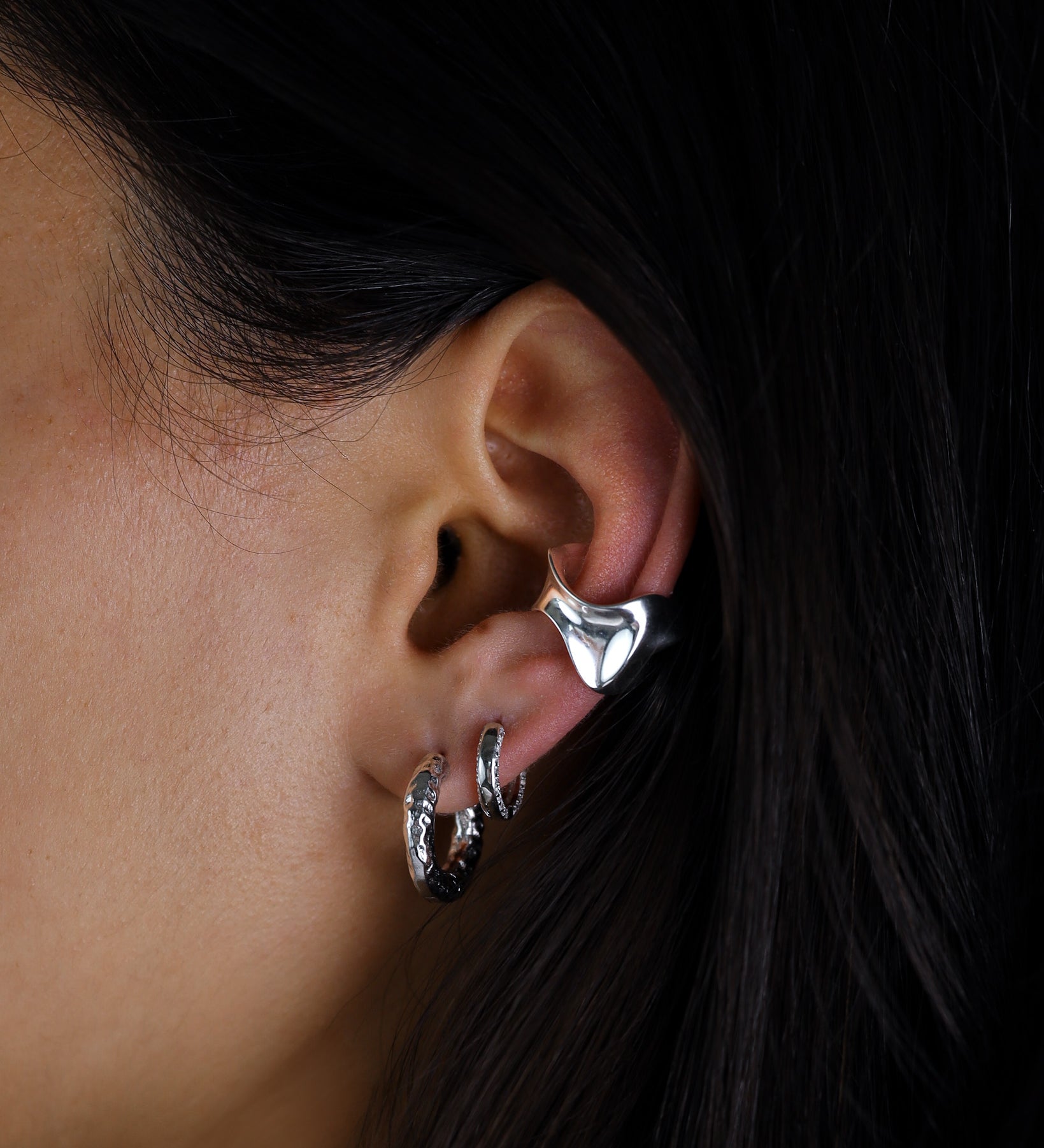 Close-up of an ear wearing silver hoop earrings with a dark background