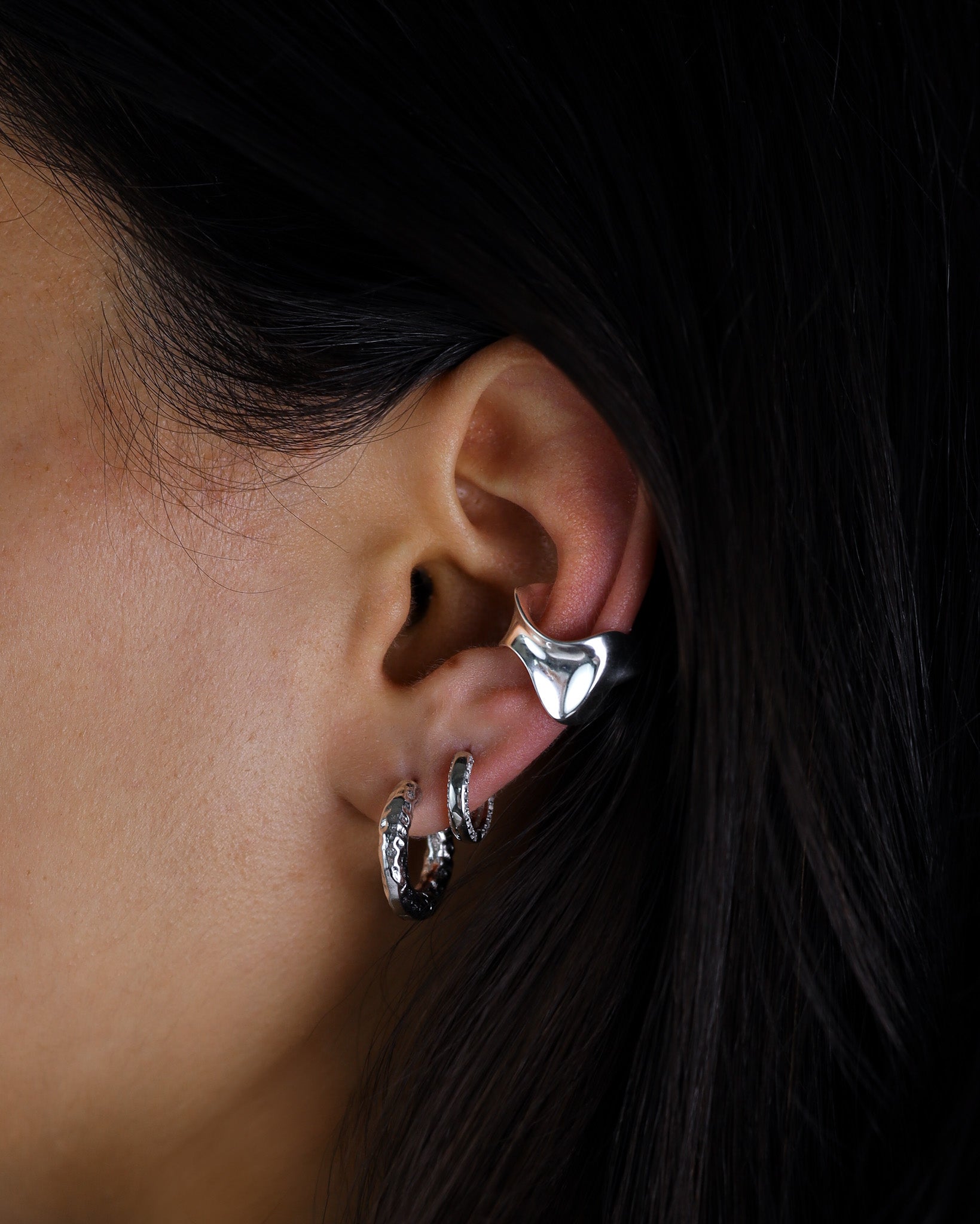 Close-up of an ear wearing silver hoop earrings with a dark background