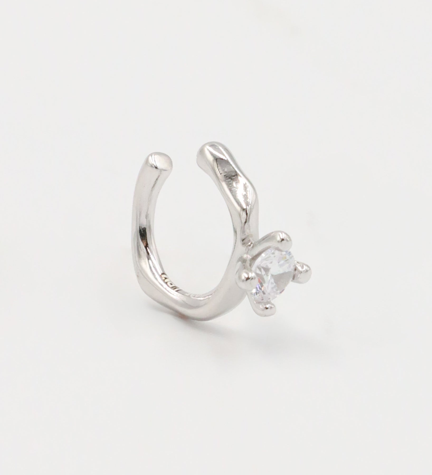 A silver ring with a round band and a central, square-shaped, transparent crystal embellishment.