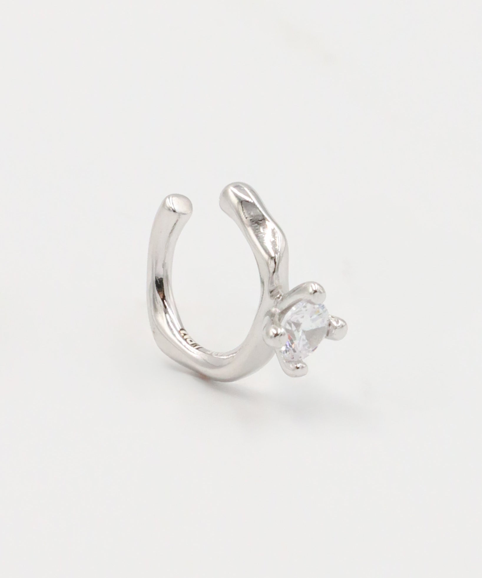 A silver ring with a round band and a central, square-shaped, transparent crystal embellishment.