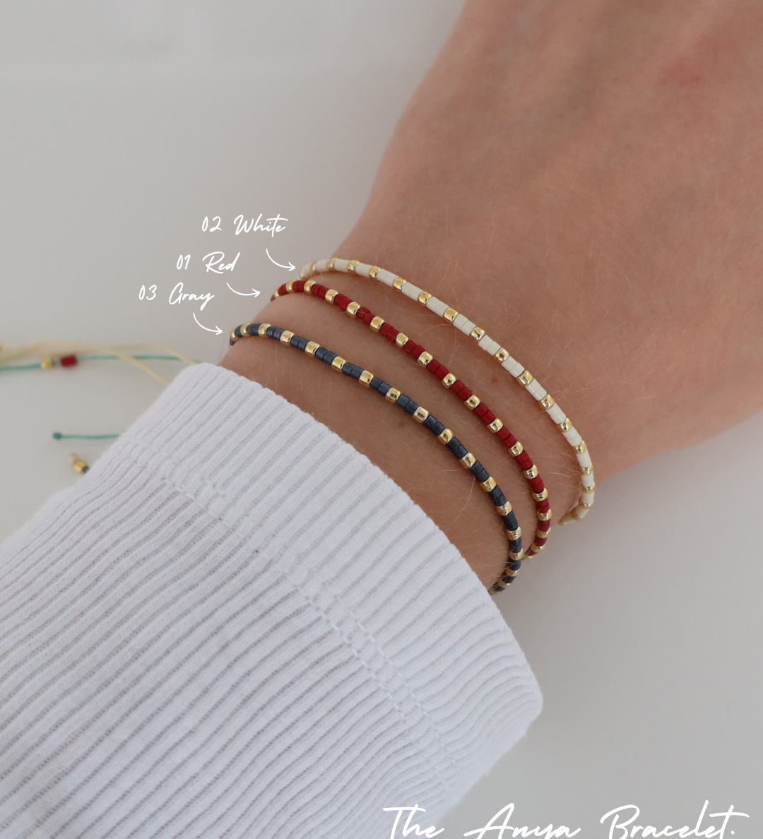 Close-up of a wrist wearing three delicate beaded Anya bracelets in different color combinations, styled together with a white ribbed sleeve.
