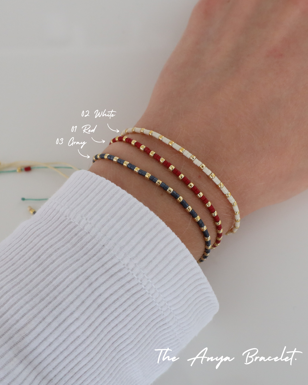 Close-up of a wrist wearing three delicate beaded Anya bracelets in different color combinations, styled together with a white ribbed sleeve.