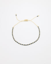 Flat-lay image of the Anya bracelet featuring alternating dark and gold beads, strung on a cream cord with an adjustable sliding closure.