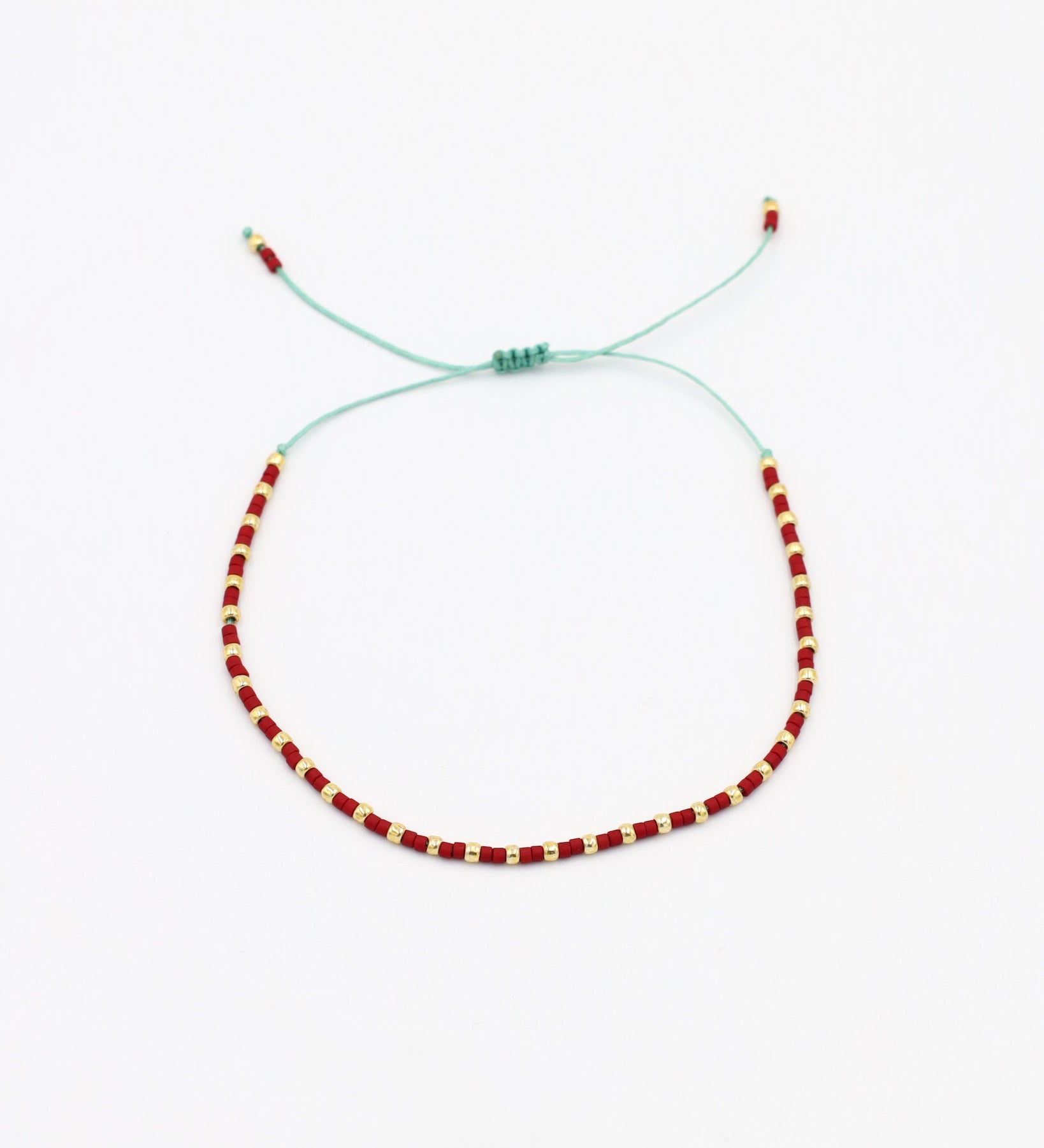 An adjustable bracelet with gold and red beads and rhinestones on a white background.
