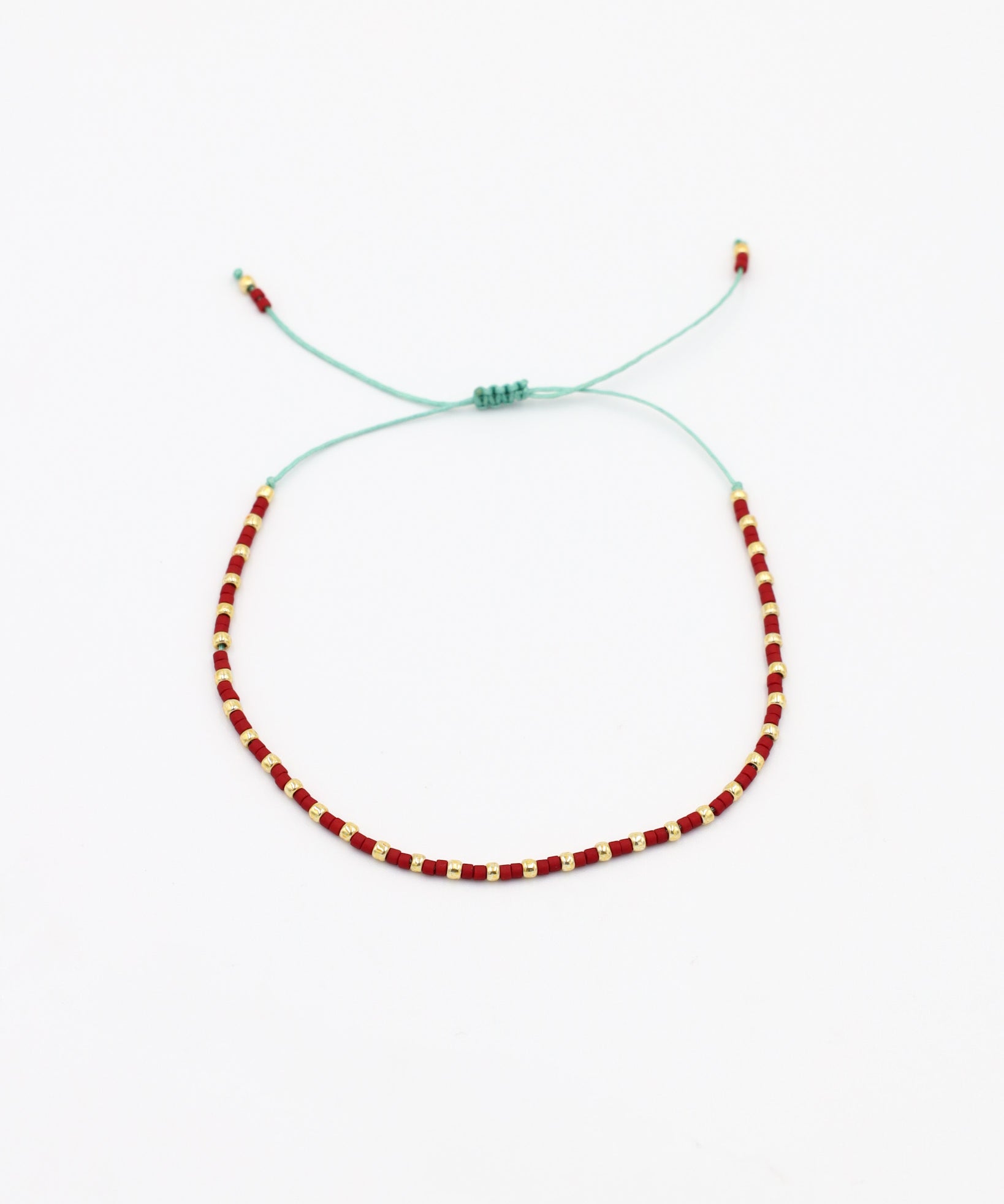 An adjustable bracelet with gold and red beads and rhinestones on a white background.