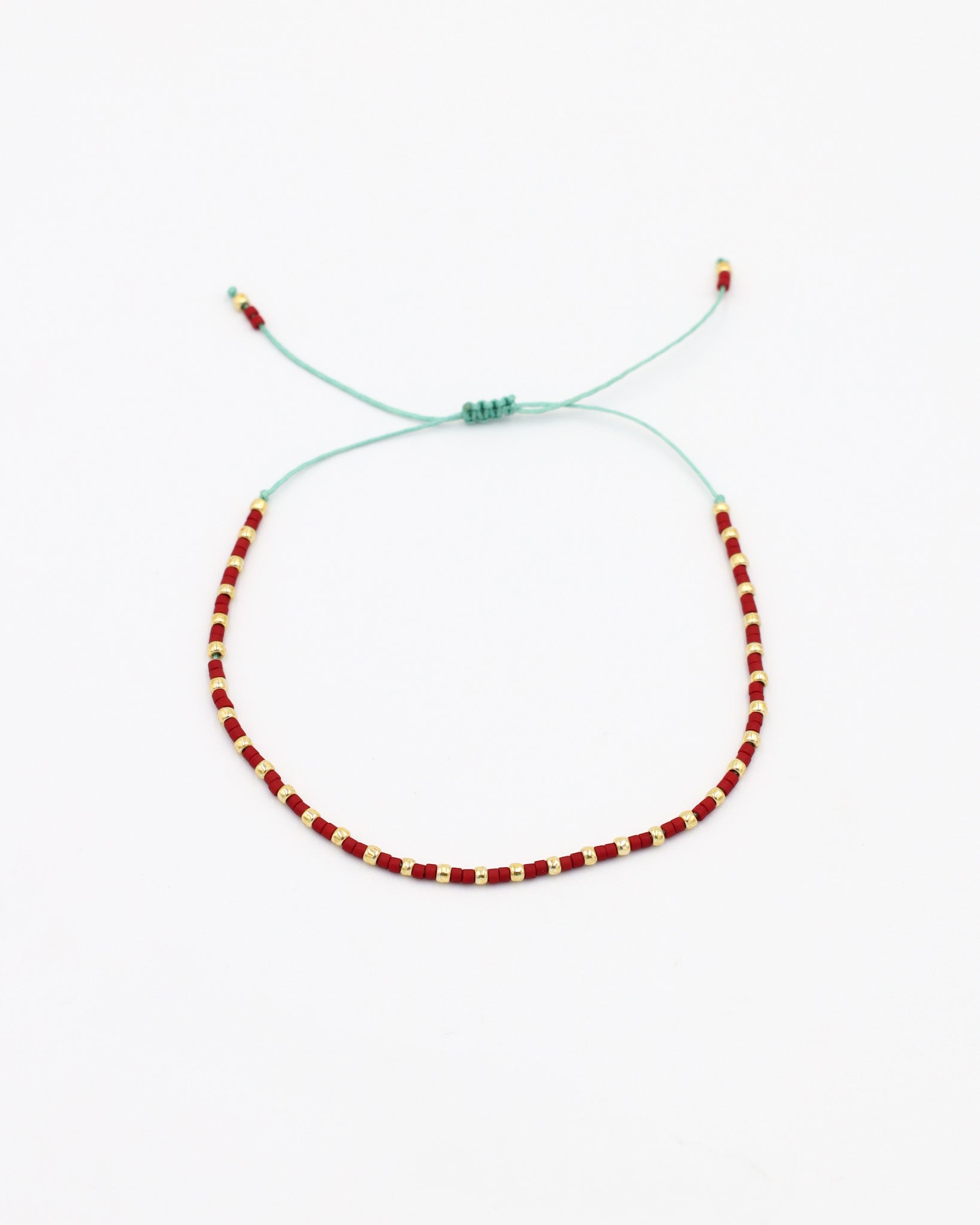 An adjustable bracelet with gold and red beads and rhinestones on a white background.